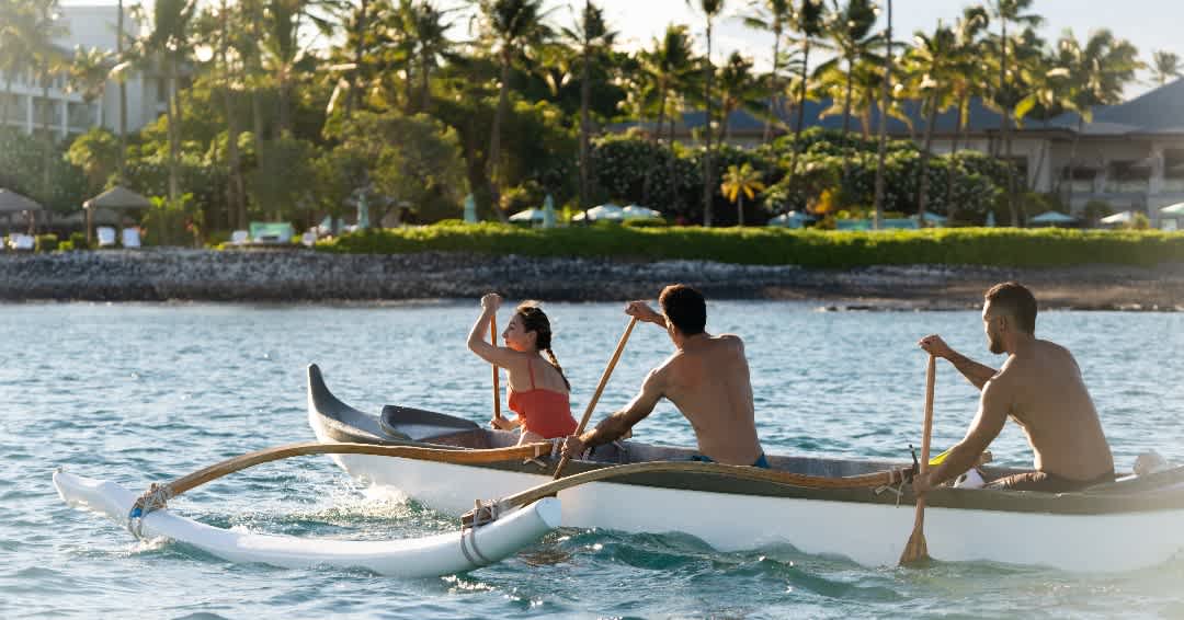 People paddling an outrigger canoe near the shore of the Kohala Coast.