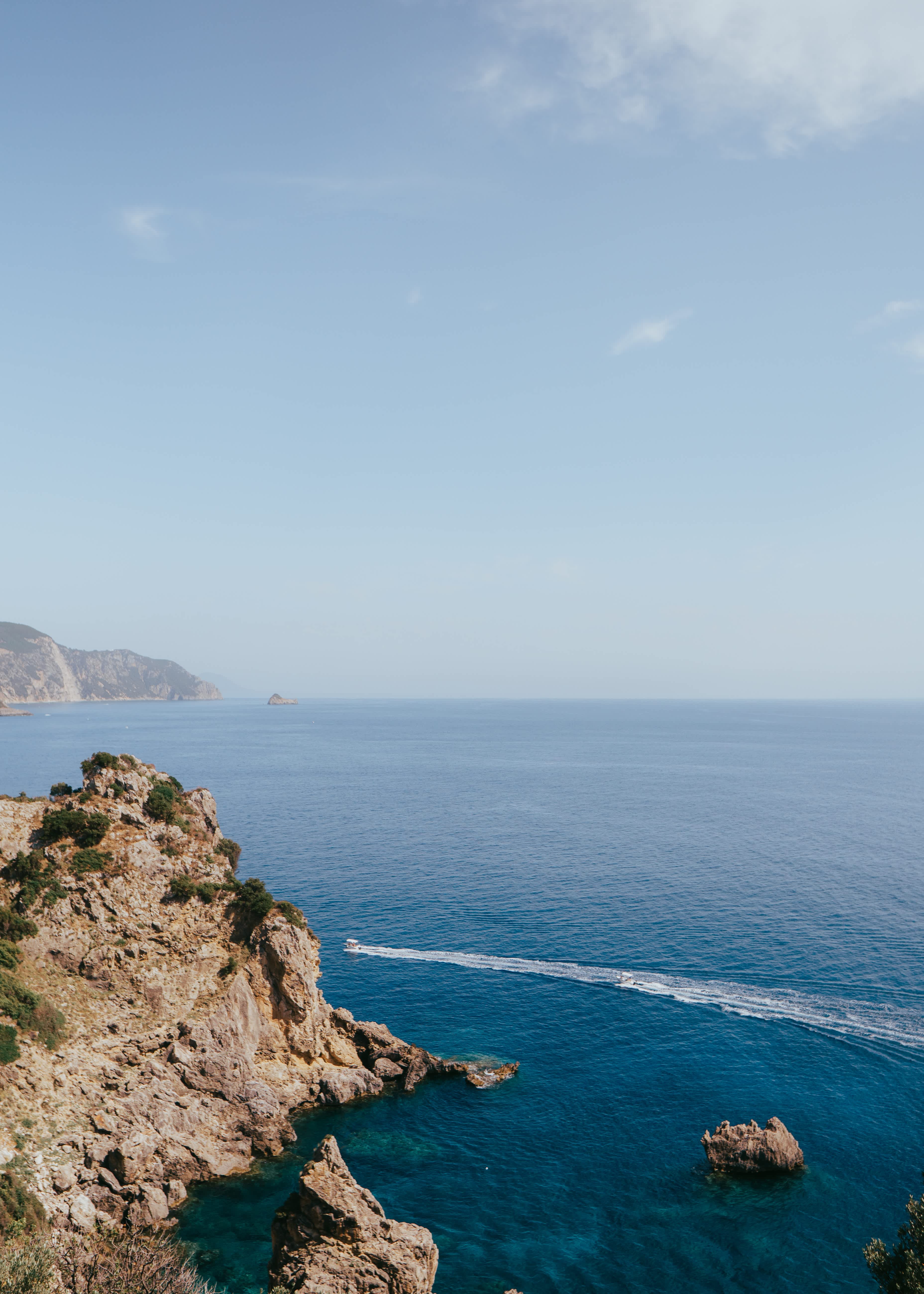 Rocky coastline of Corfu with a view of the blue sea and distant cliffs.