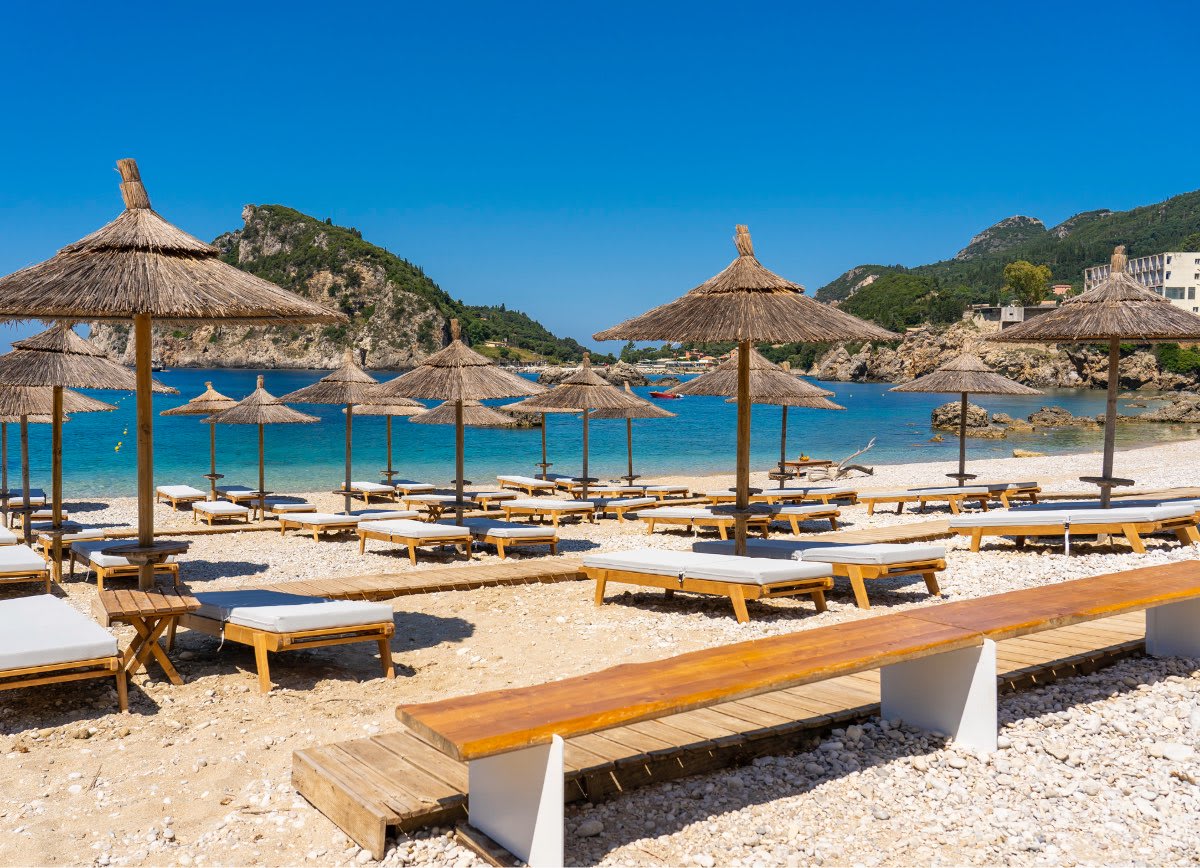 Akron Beach Bar in Corfu with straw umbrellas and lounge chairs facing the turquoise sea.