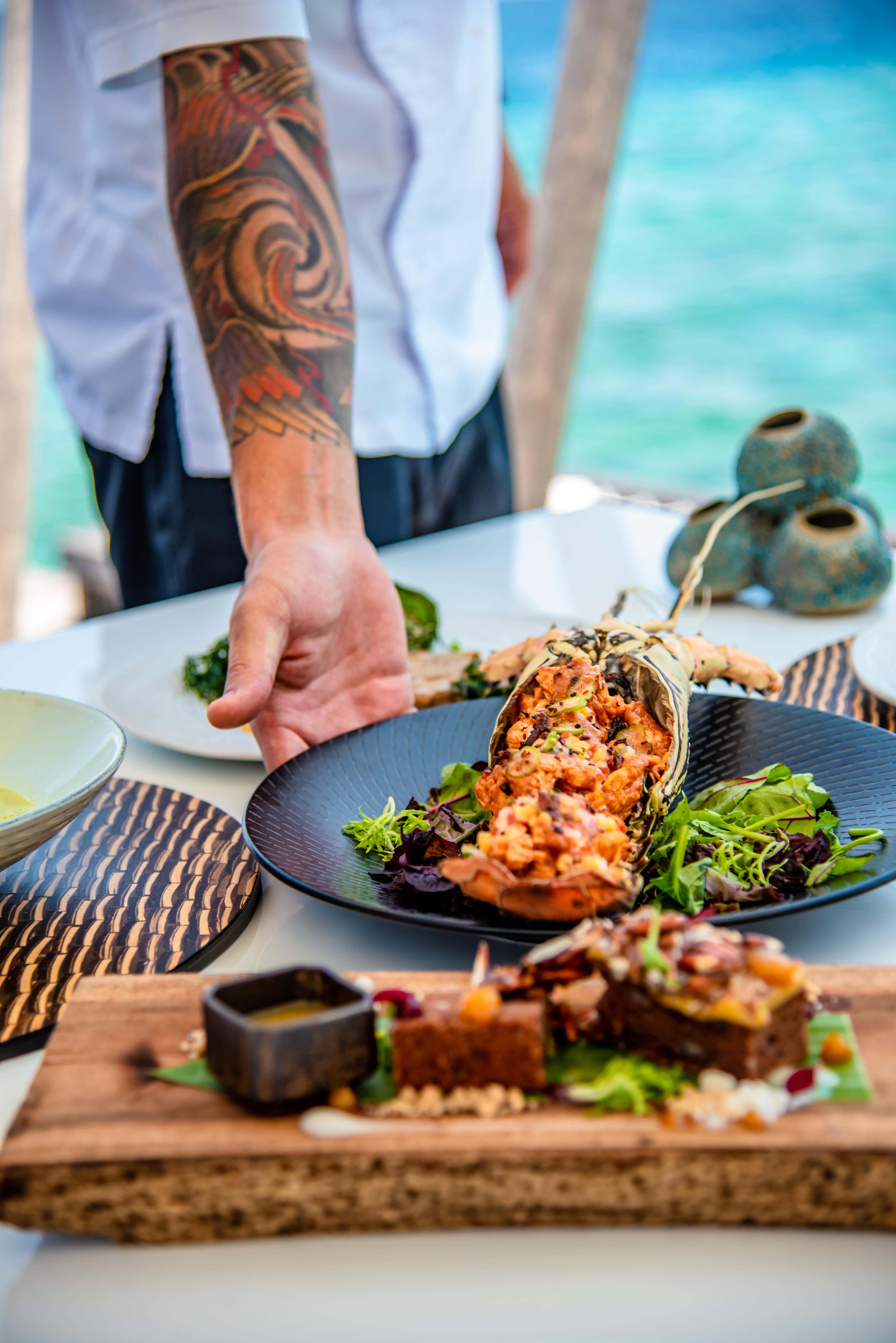 Chef serving a gourmet lobster dish with salad at an oceanfront restaurant.