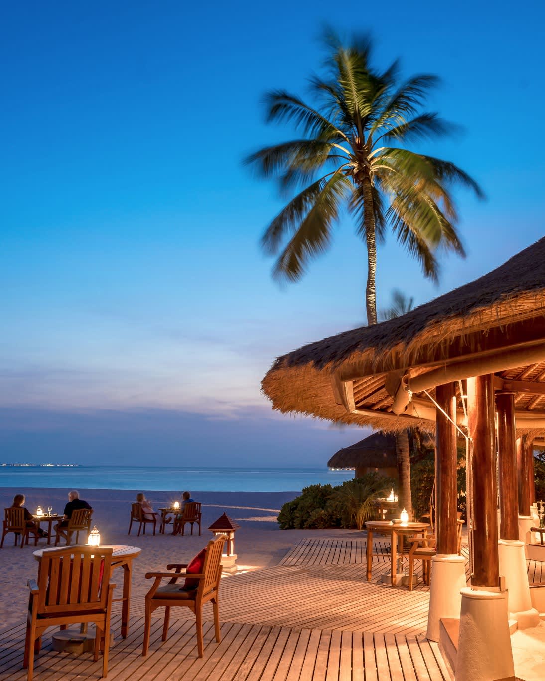 An outdoor beachfront dining area with palm trees and a serene ocean backdrop at Vabbinfaru Banyan Tree Resort in the Maldives.