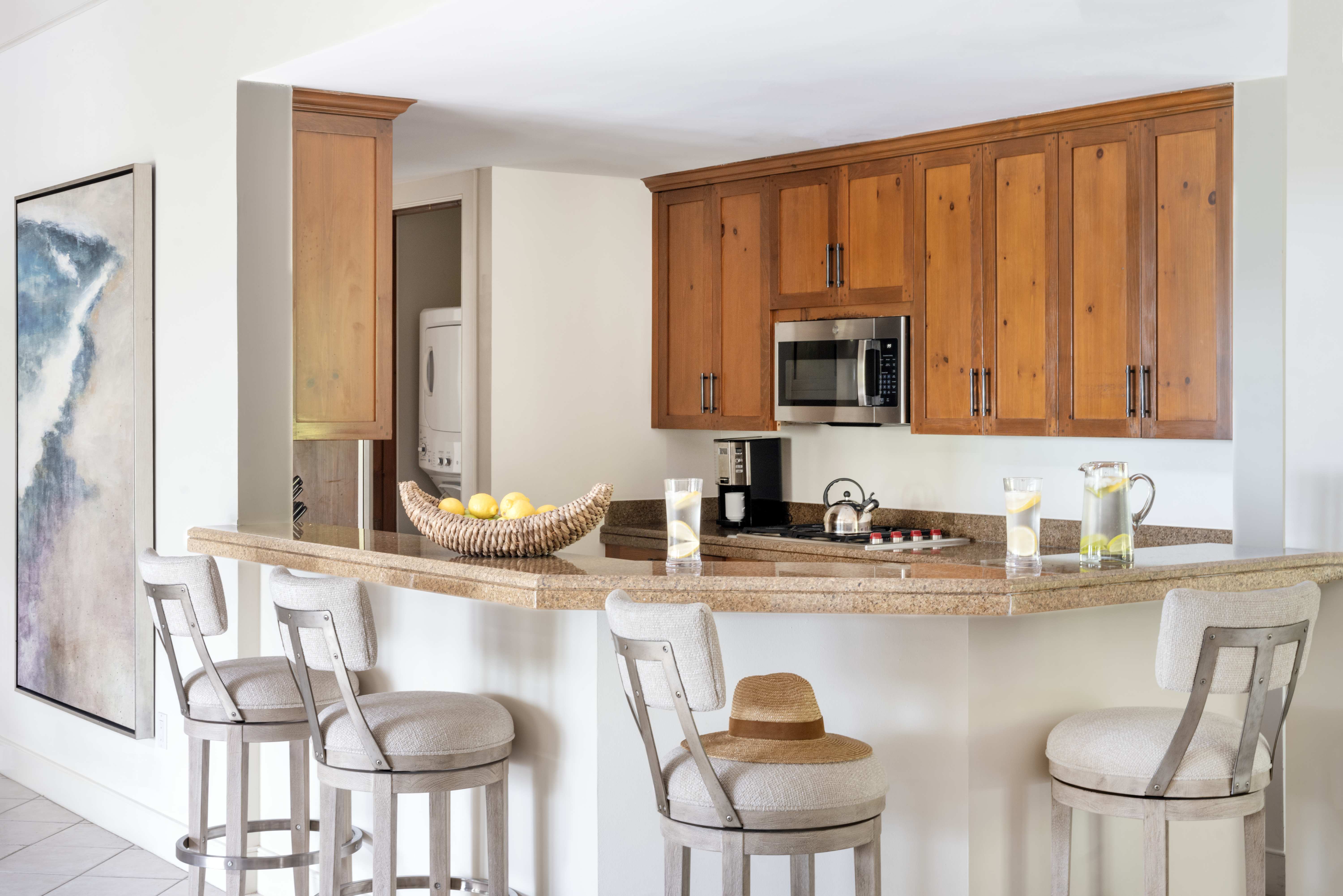The kitchen of an Exclusive Resorts property at The Abaco Club, featuring warm wood cabinetry, granite countertops, and bar-style seating, complemented by a neutral color palette and a spacious design.