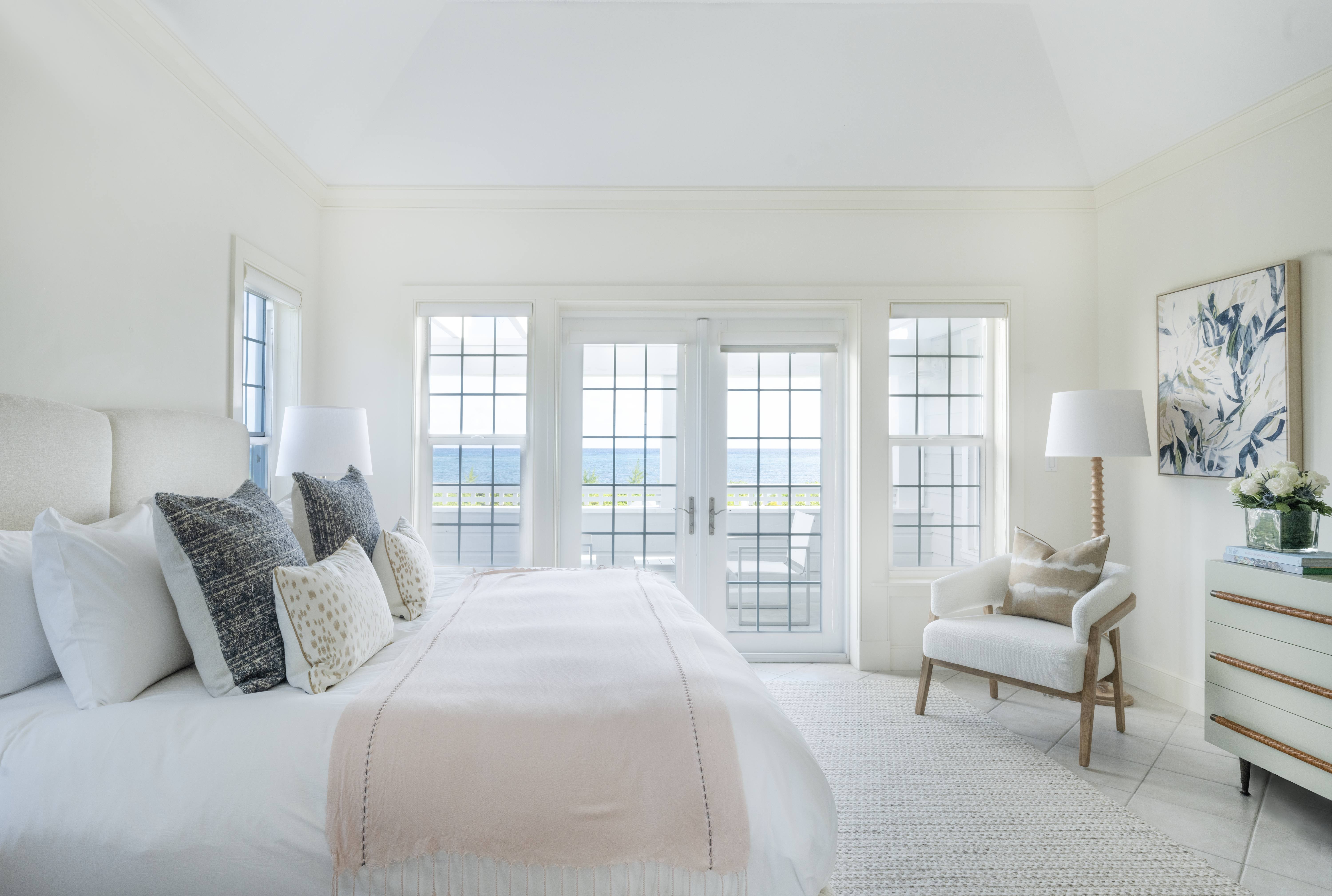 The bedroom of an Exclusive Resorts property at The Abaco Club, with a king-sized bed, elegant decor, a soft pastel palette, and a balcony offering ocean views.