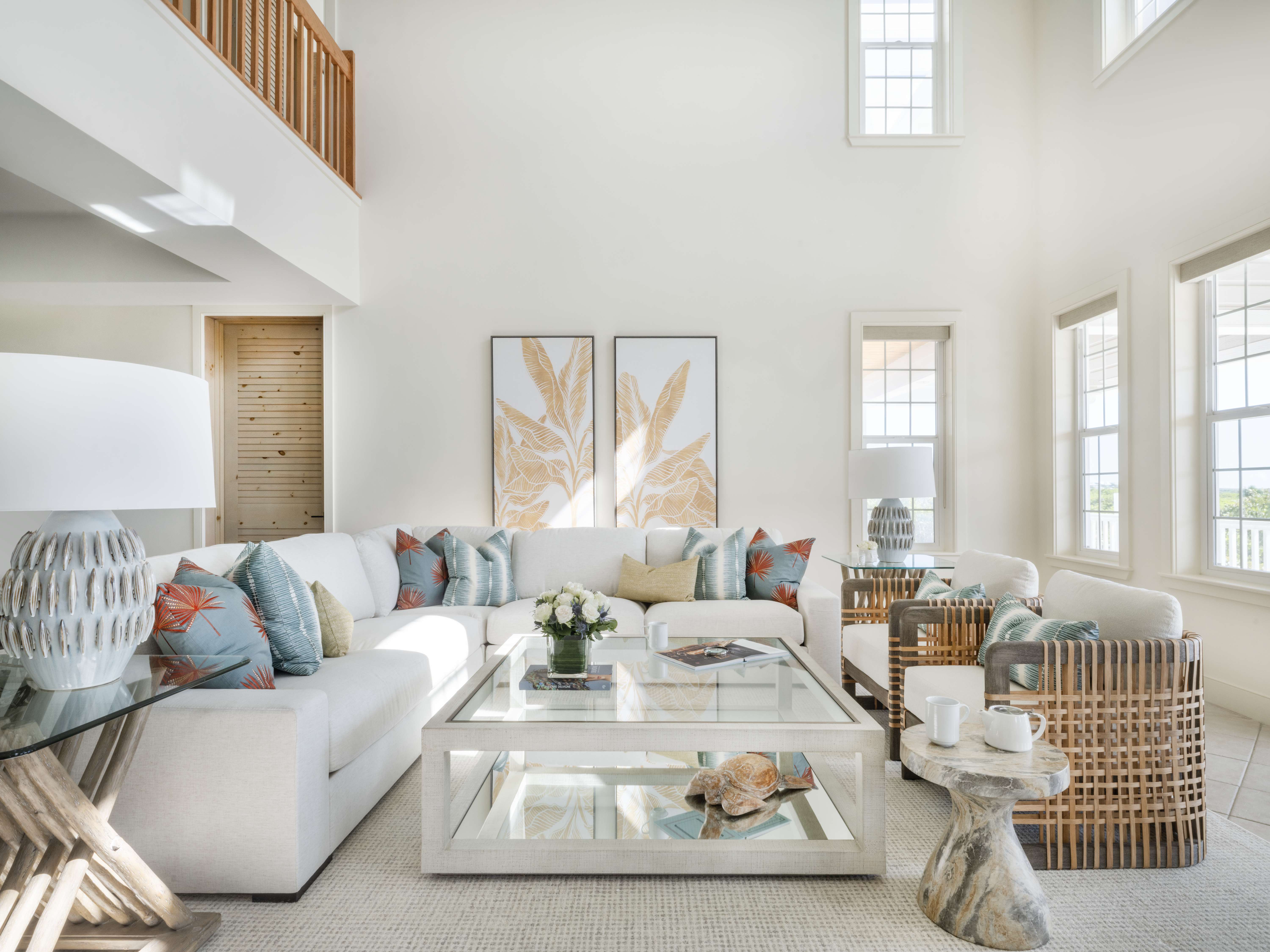 The living room at The Abaco Club Exclusive Resort property, featuring a white sectional sofa adorned with cushions, a glass coffee table with coral decorations, and high ceilings with ample natural light.