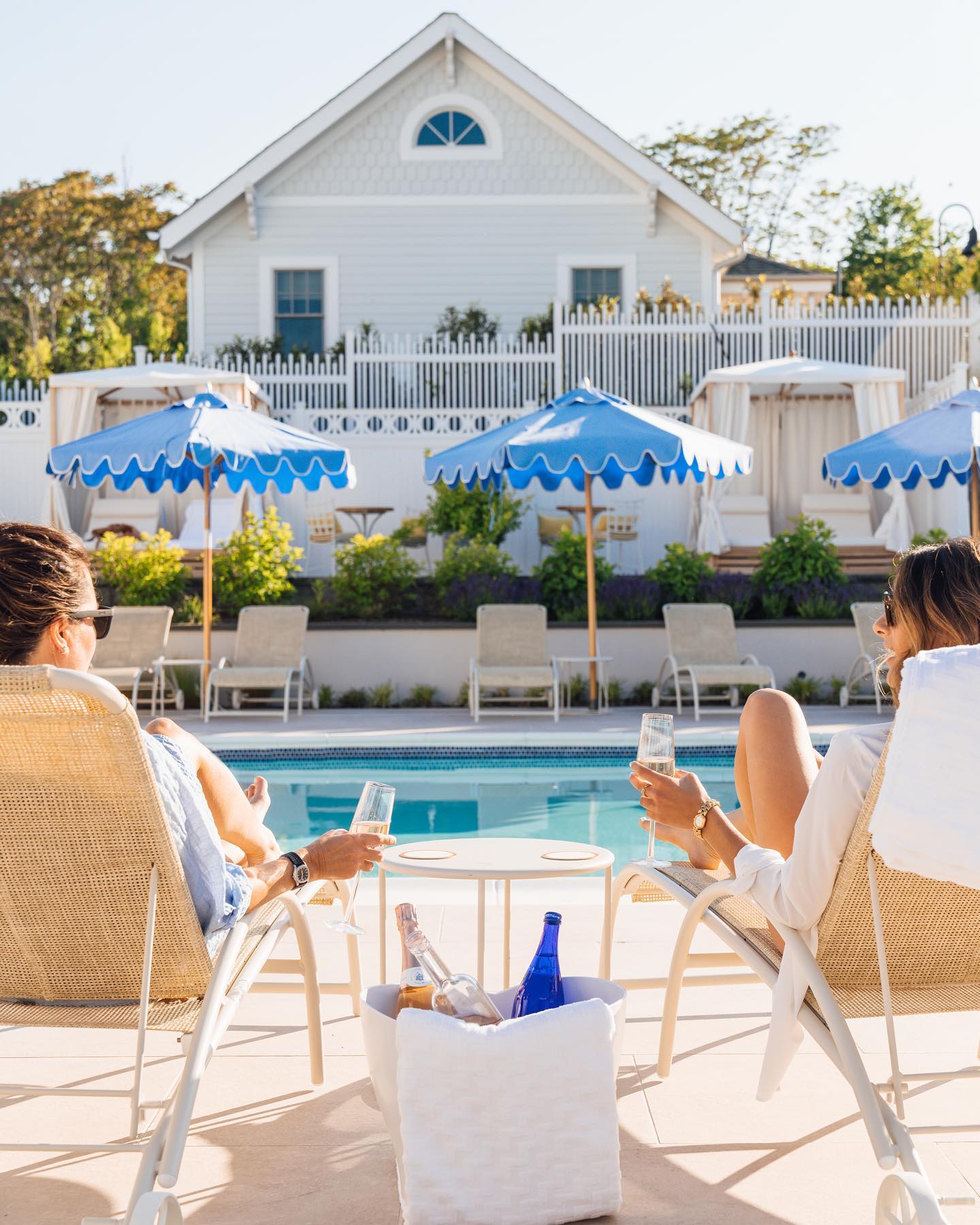 Two people relaxing by the pool with champagne, under blue umbrellas, at a serene resort setting.