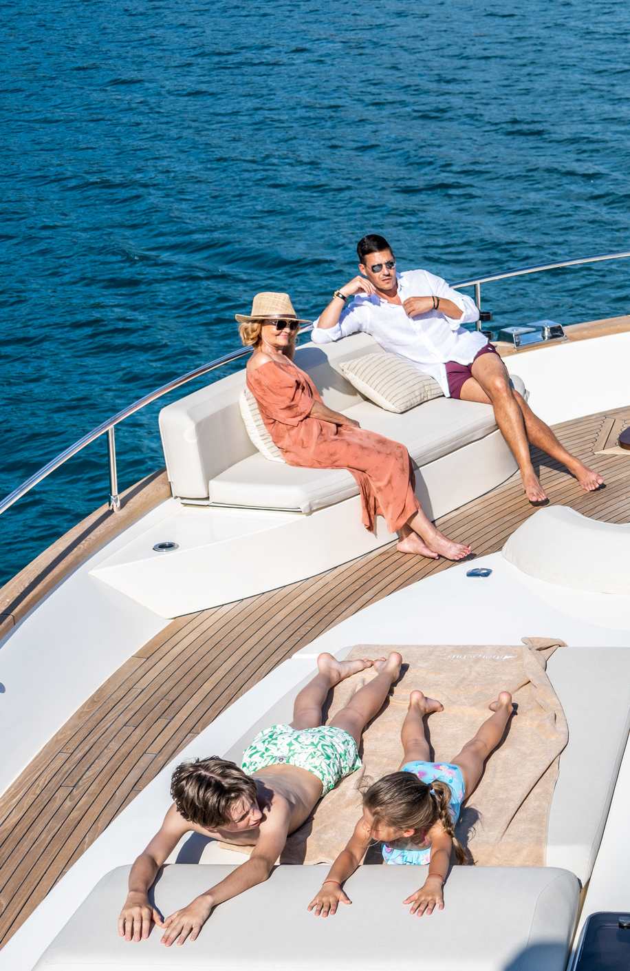 Exclusive Resorts' Members relaxing on the deck of a yacht, with two children sunbathing and adults seated, enjoying the ocean view.