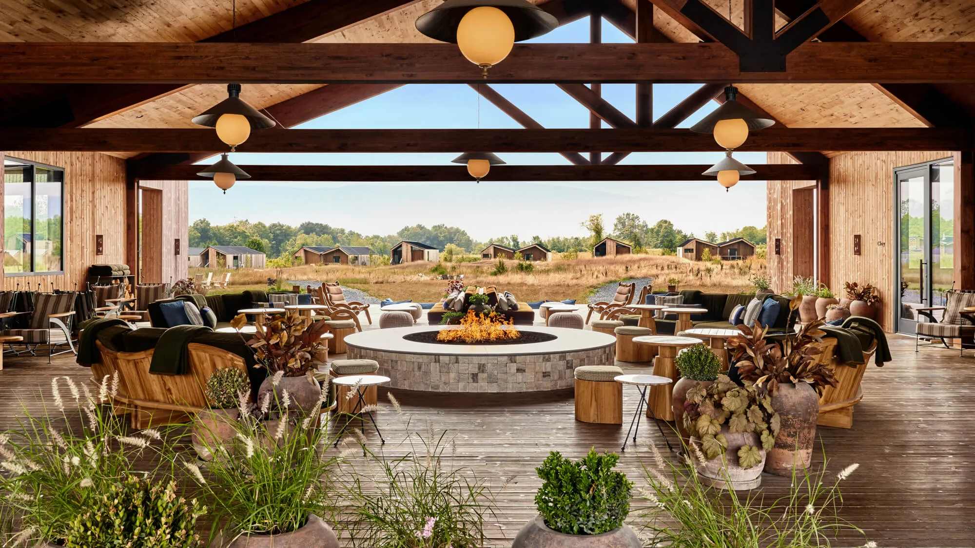 Open-air lounge with wooden beams, central fire pit, and desert landscape view in the background.