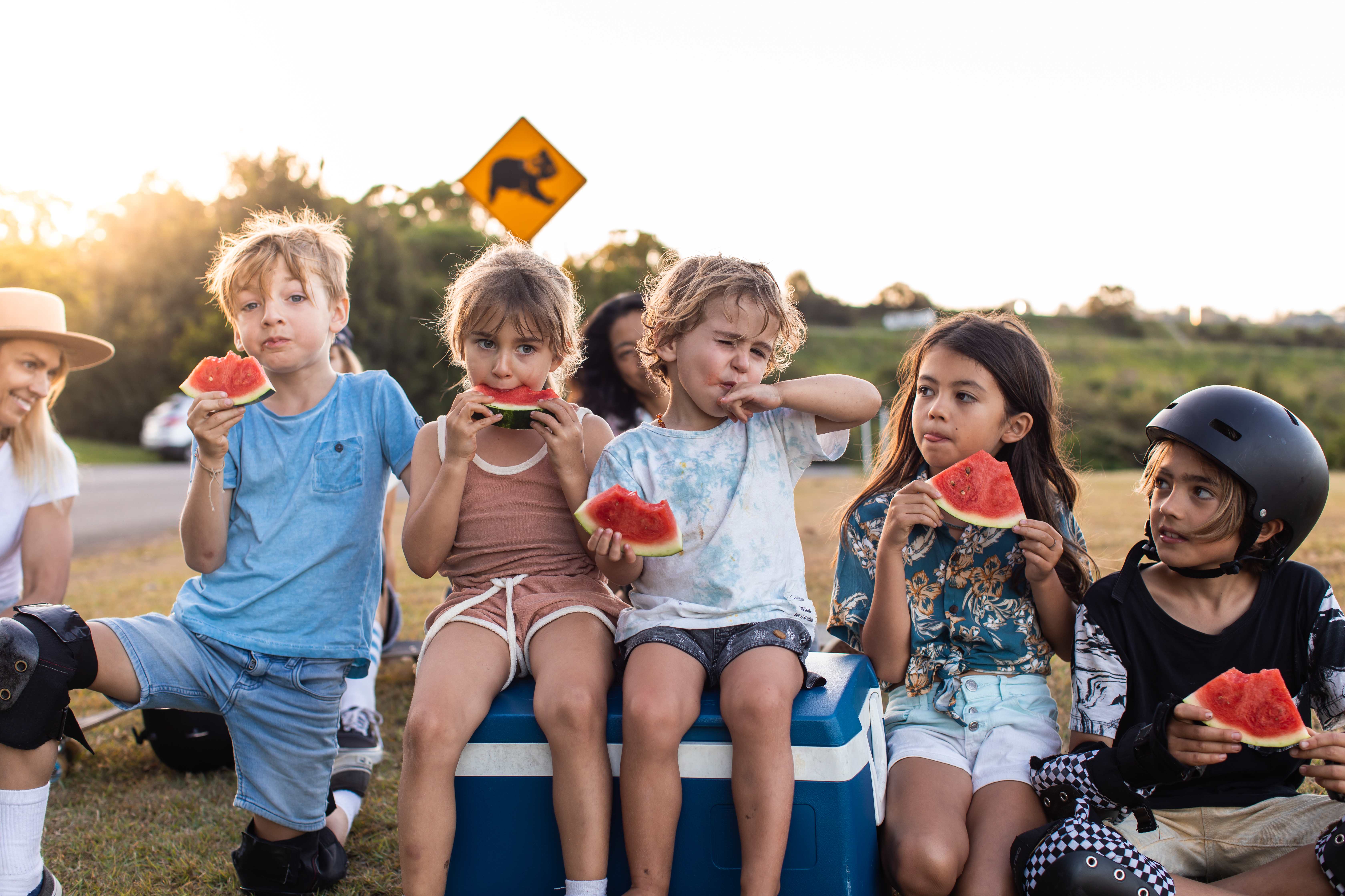 Children sitting outdoors, enjoying slices of watermelon on a sunny day.