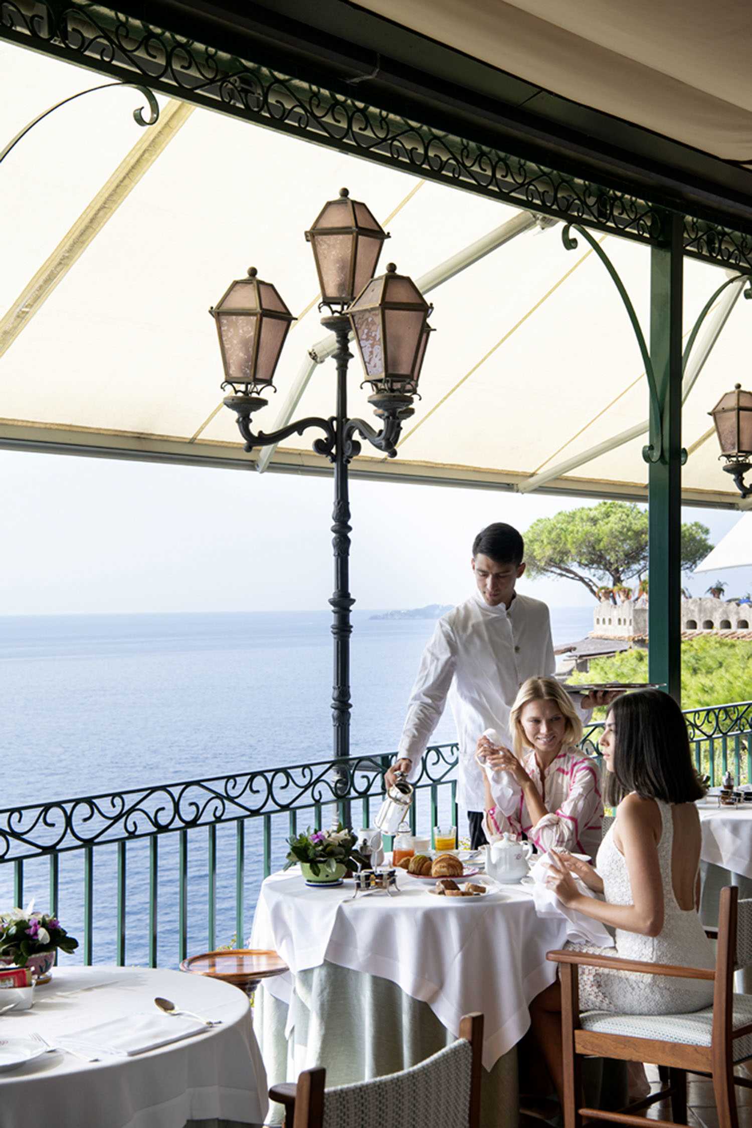 Two women being served breakfast on a terrace overlooking the Amalfi Coast.