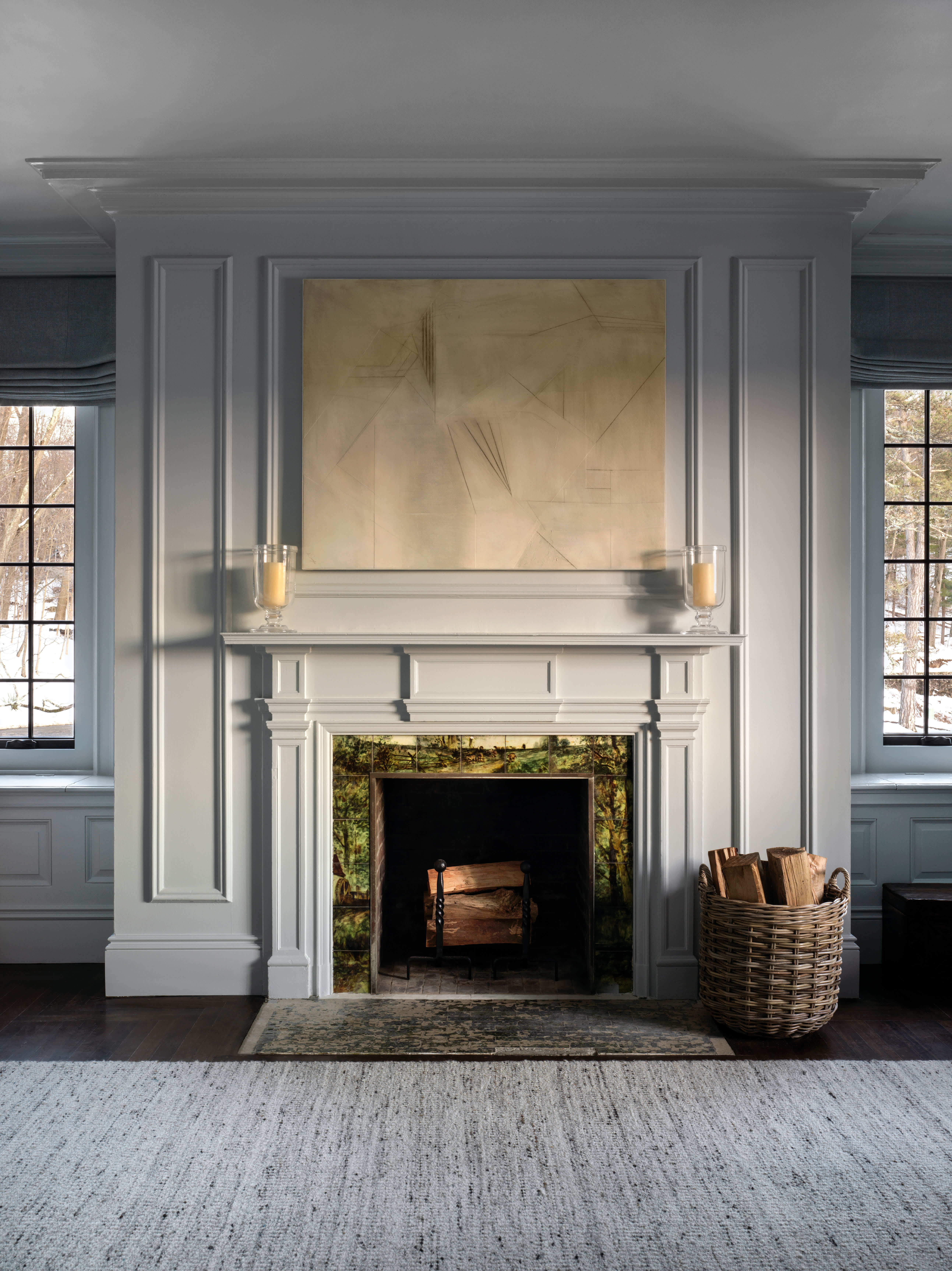 Elegant fireplace with a simple abstract painting above, wood stacked in a basket beside it, located at The Ranch Hudson Valley.