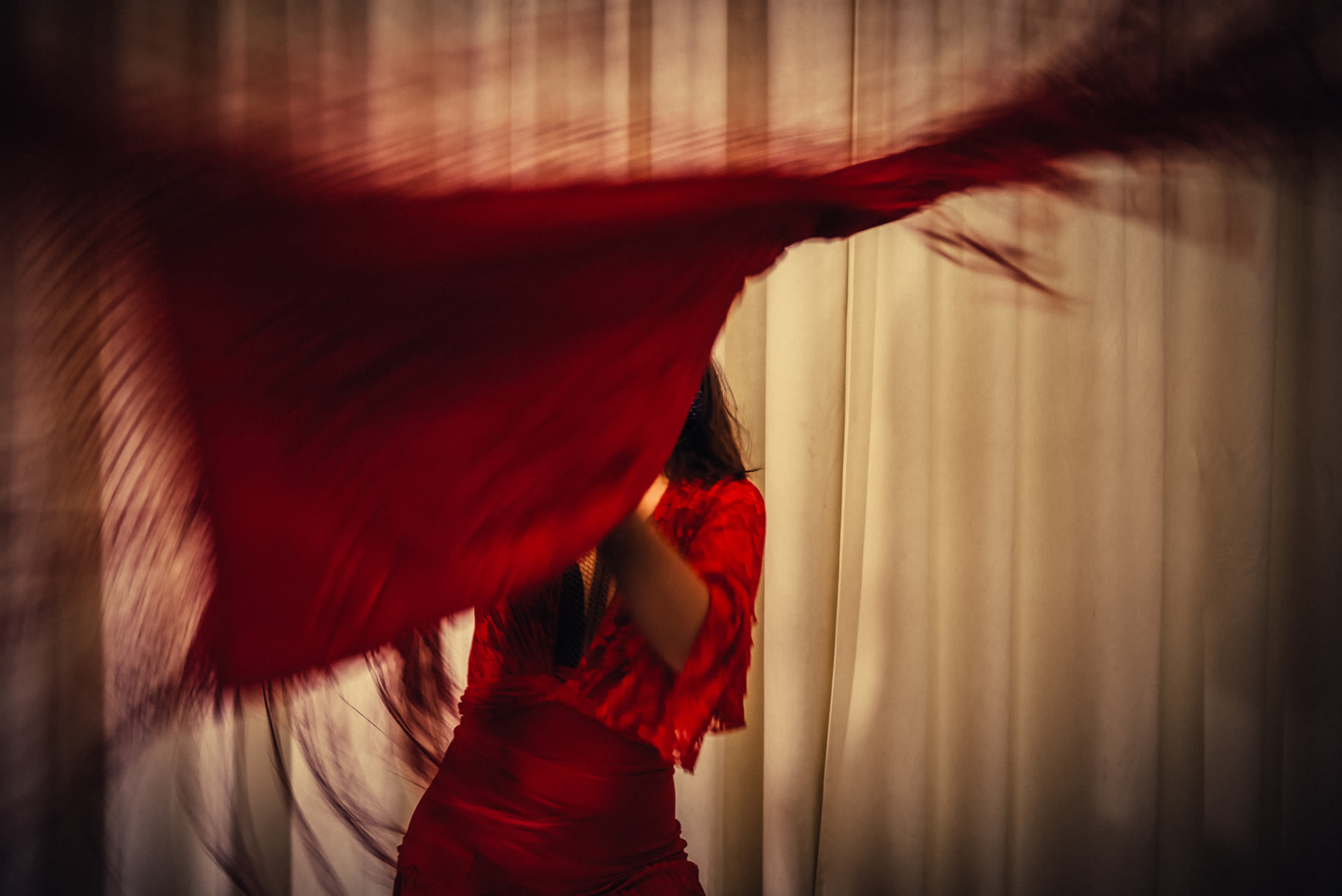 A woman dancing in a red dress while twirling a red cloth.
