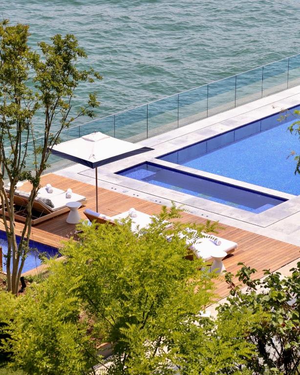 Infinity pool and lounge chairs overlooking the water, surrounded by greenery at Istanbul Peninsula Hotel.