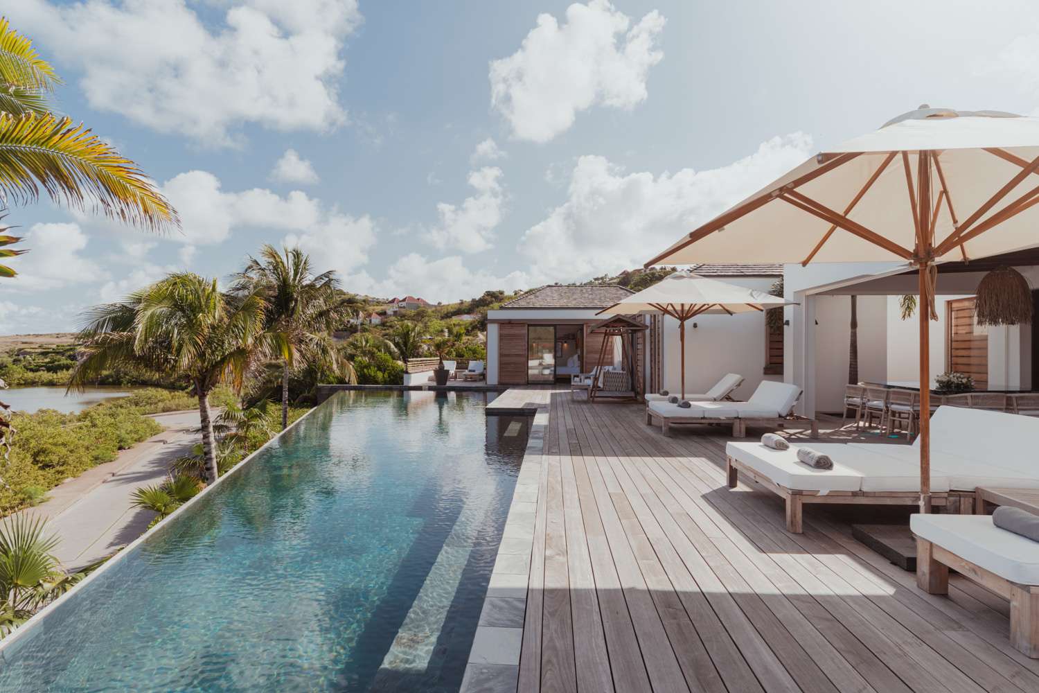 Infinity pool and sun loungers under umbrellas at Exclusive Resorts' villa in St. Barts, overlooking lush greenery and a peaceful landscape.