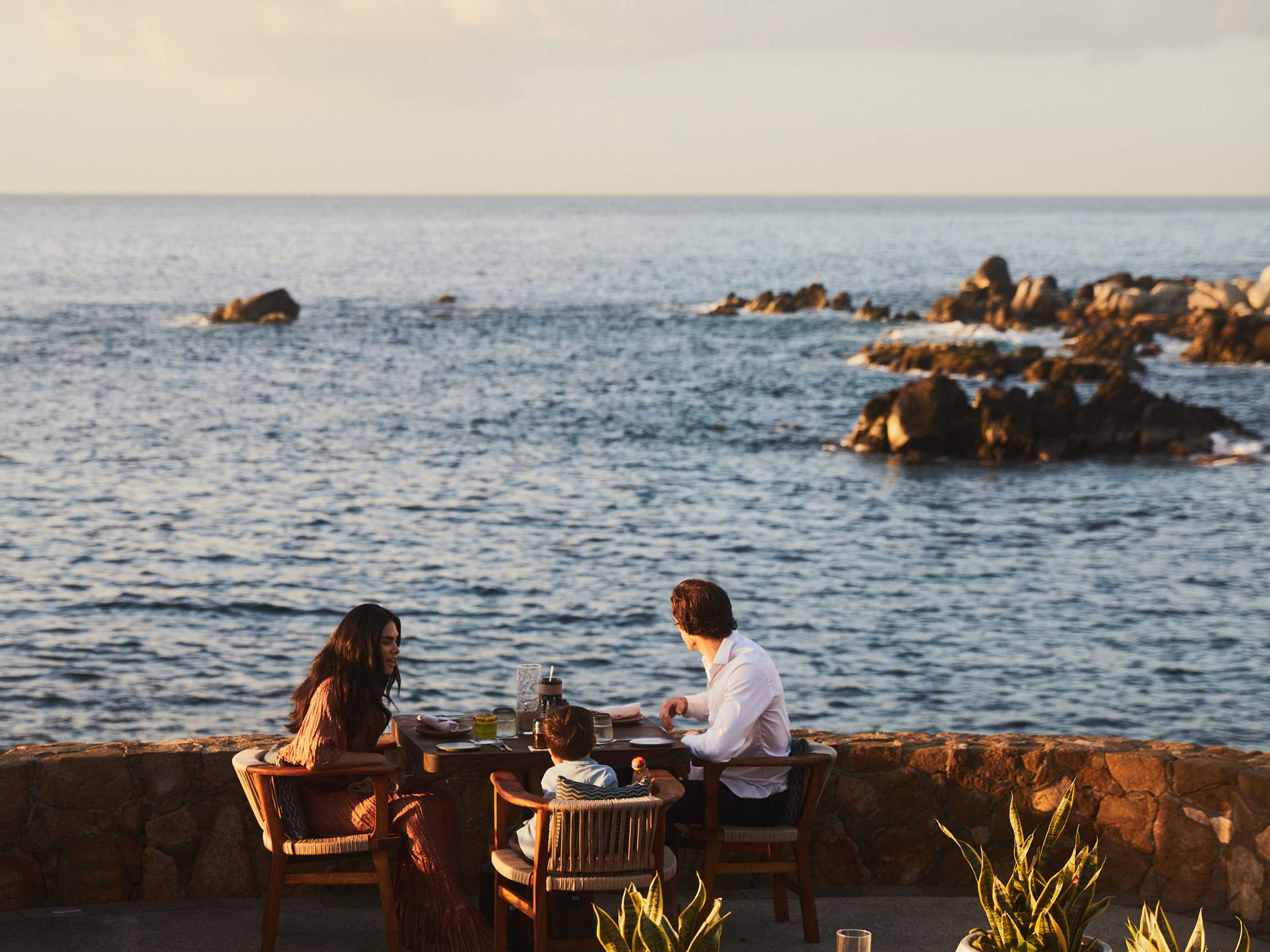 Family dining outdoors with an ocean view at Esperanza in Los Cabos, Mexico, during sunset.
