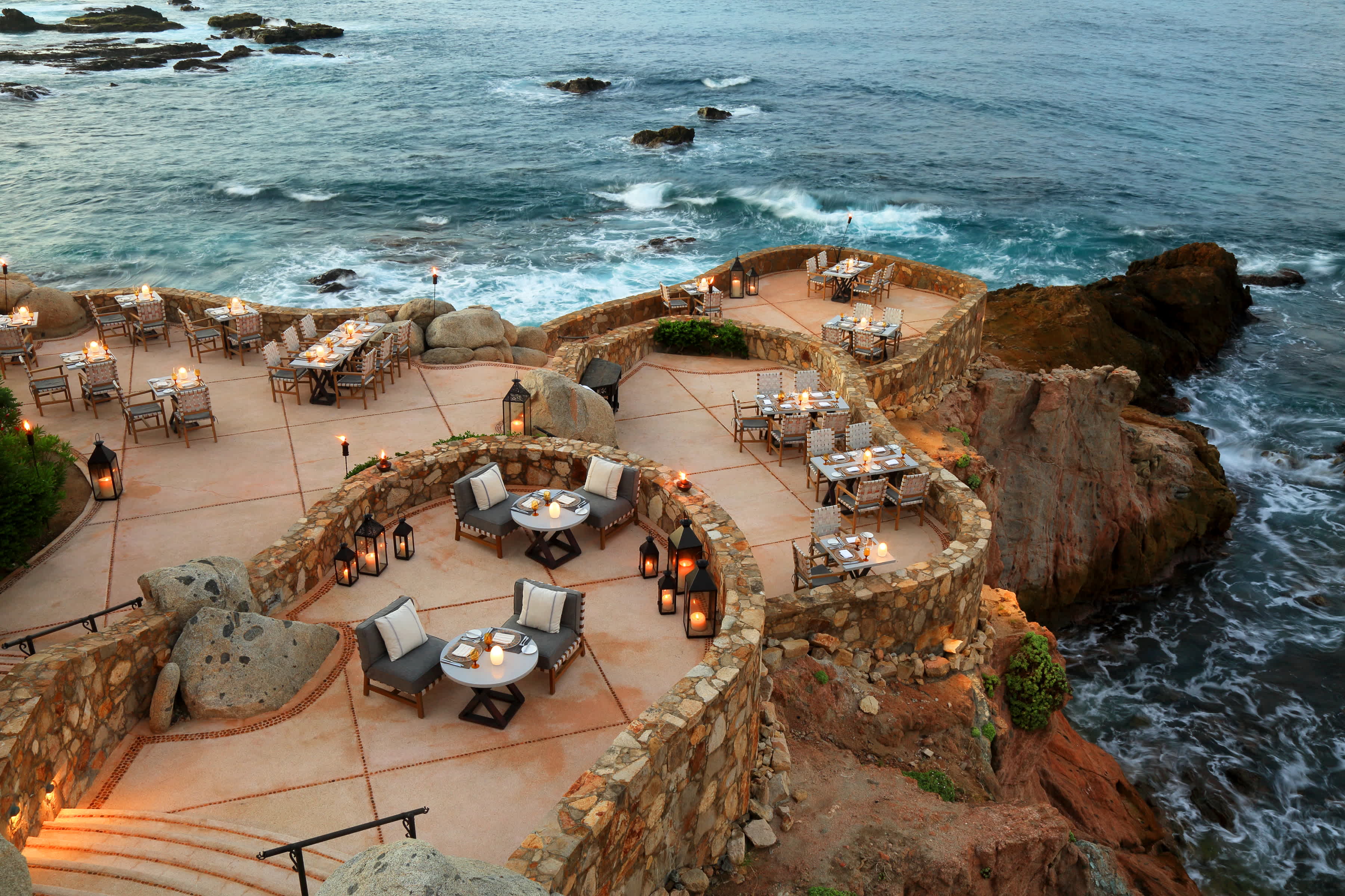 Outdoor dining area with ocean view at Esperanza in Los Cabos, Mexico, with tables set and lanterns for evening ambiance.