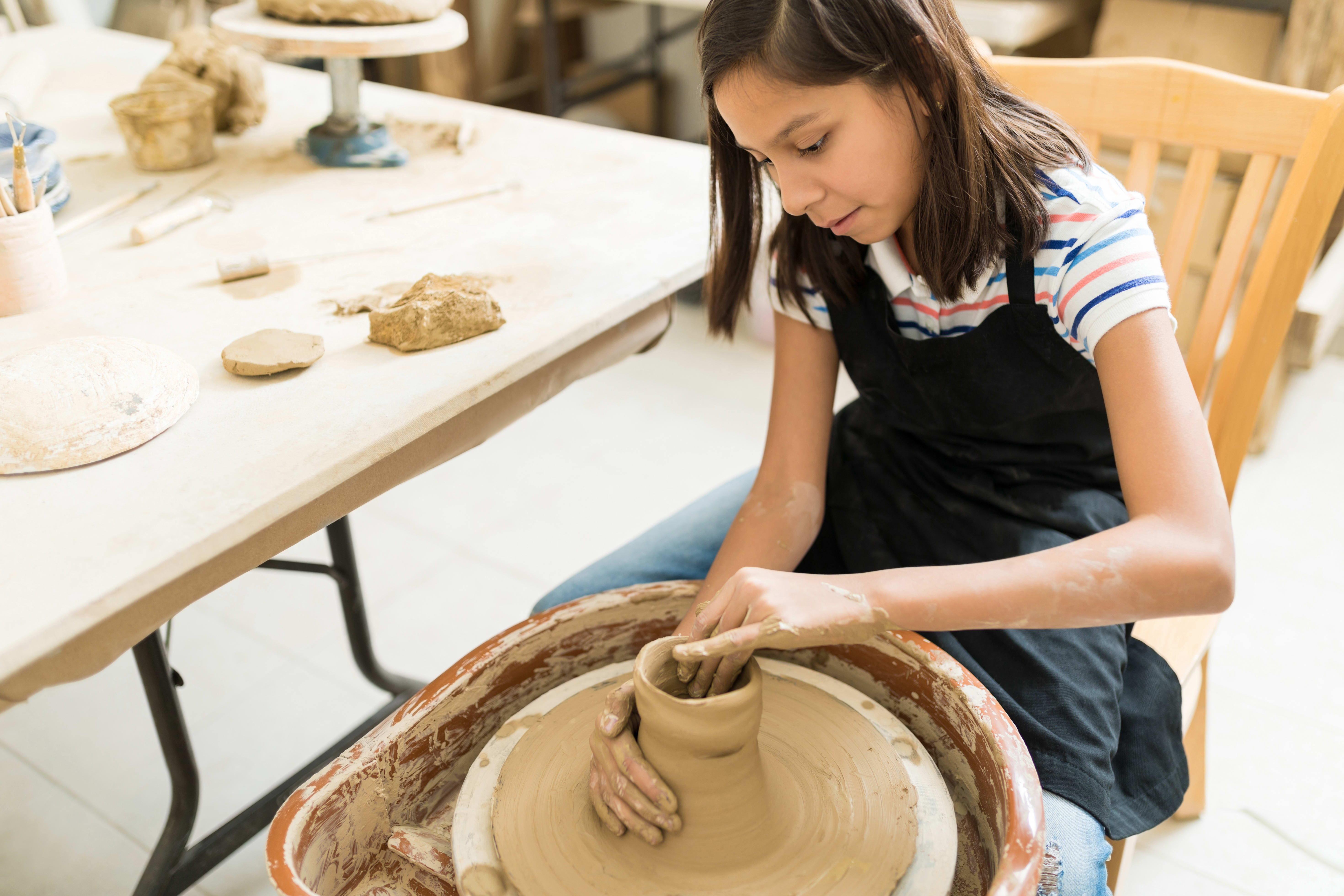A kid spinning the wheel in a pottery class.