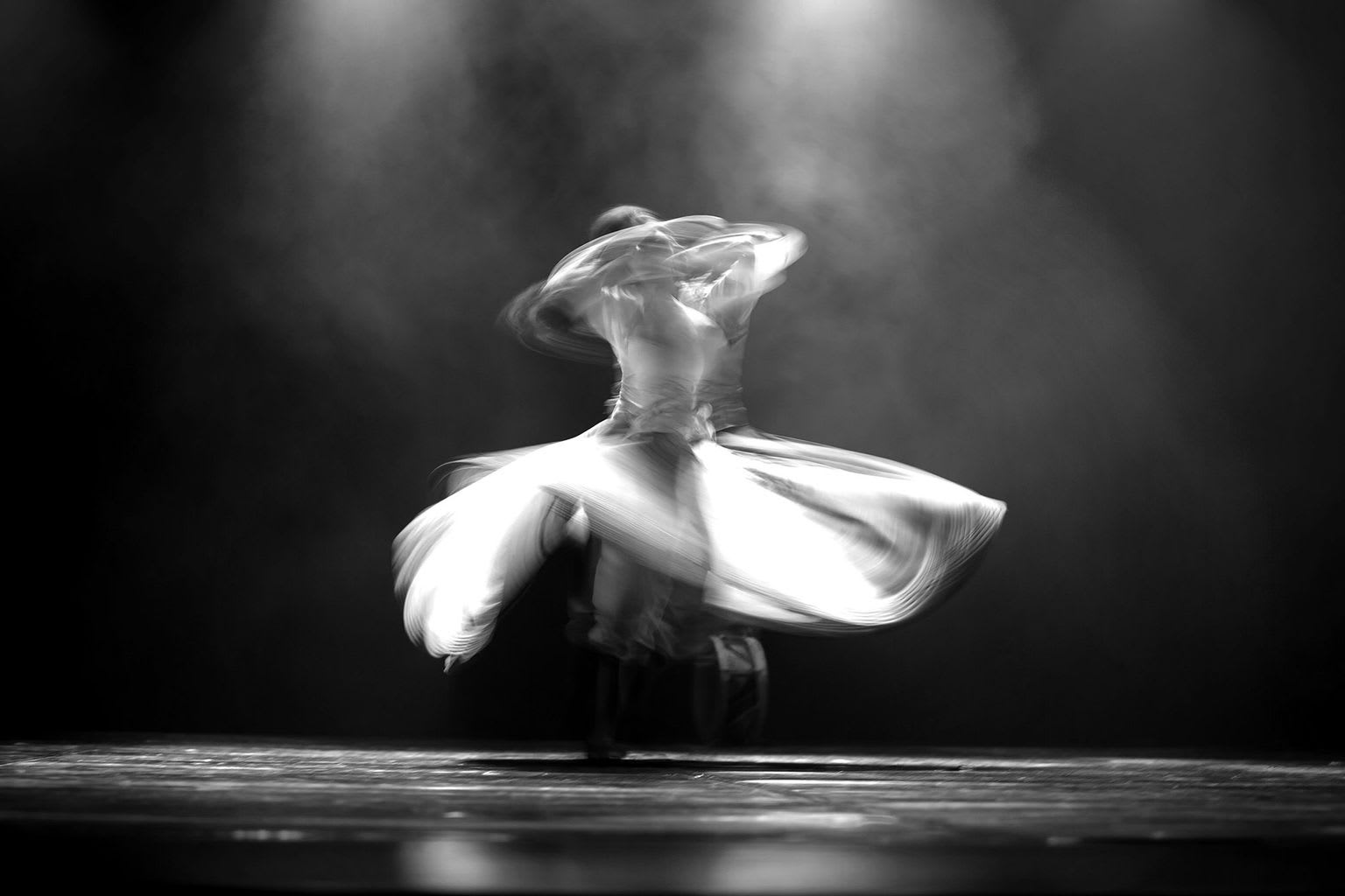 Black and white photo of a whirling dervish dancer spinning on stage.