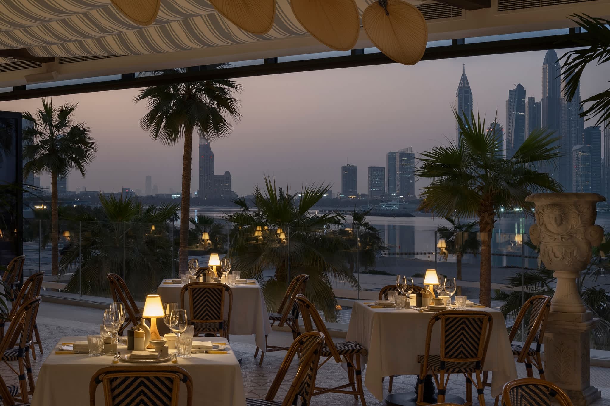 Outdoor dining setup at sunset with a view of Dubai skyline and palm trees.