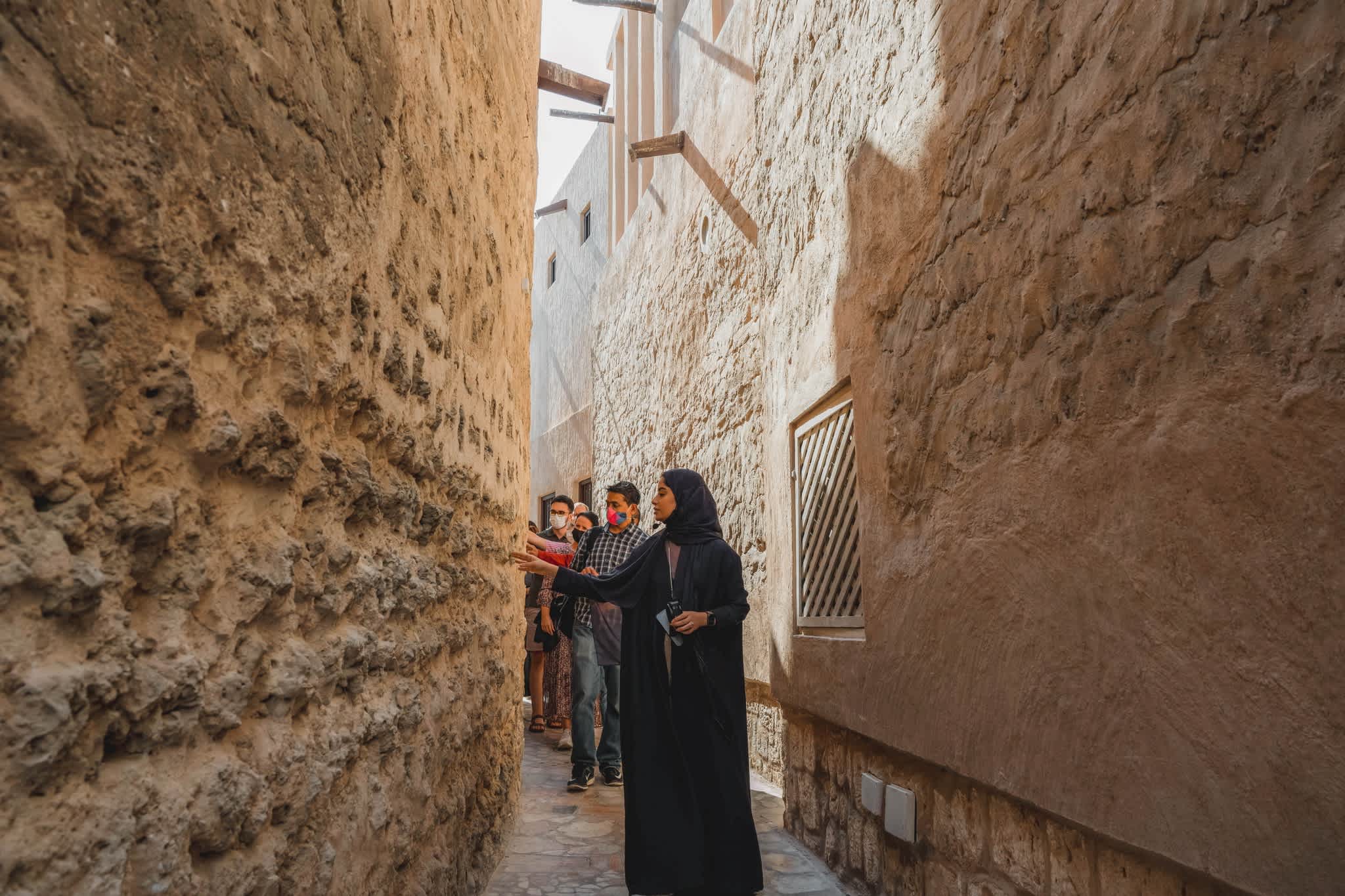 A guided tour through narrow stone alleyways of historic Dubai district with tourists exploring the architecture.