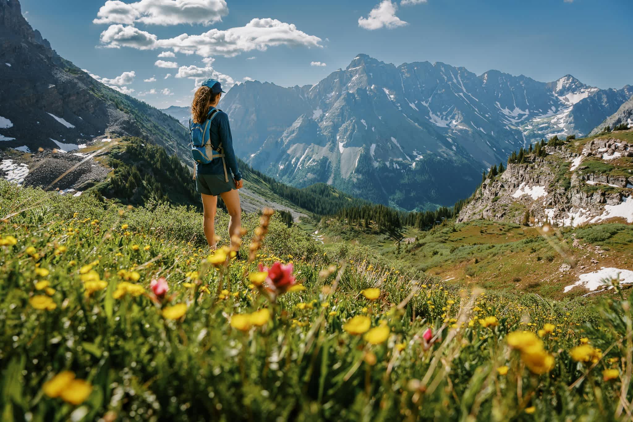 Hiker enjoying a scenic view of the Maroon Bells mountains surrounded by wildflowers in Colorado.