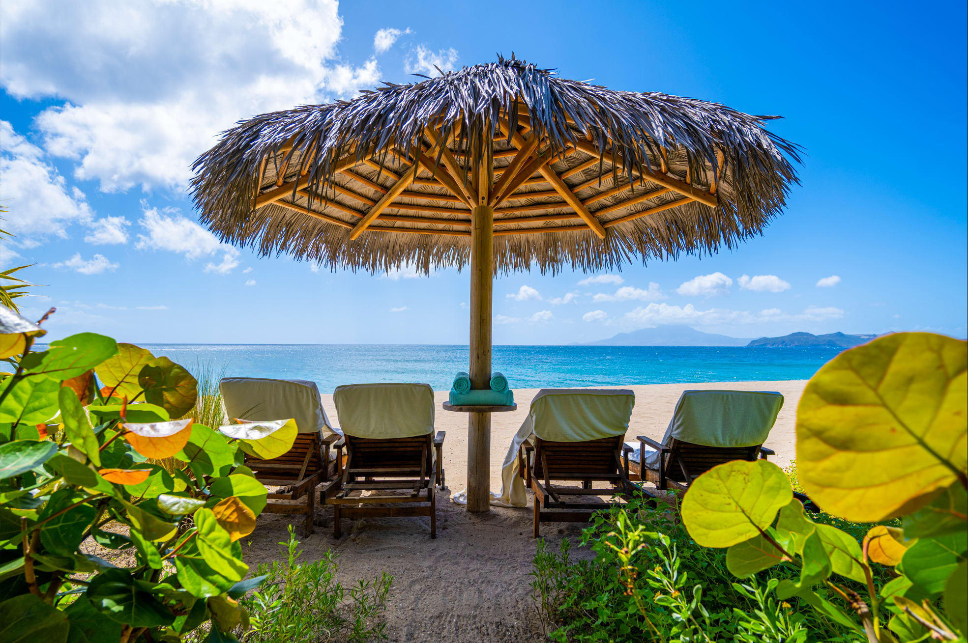 Tropical beach view in Nevis with lounge chairs under a thatched umbrella