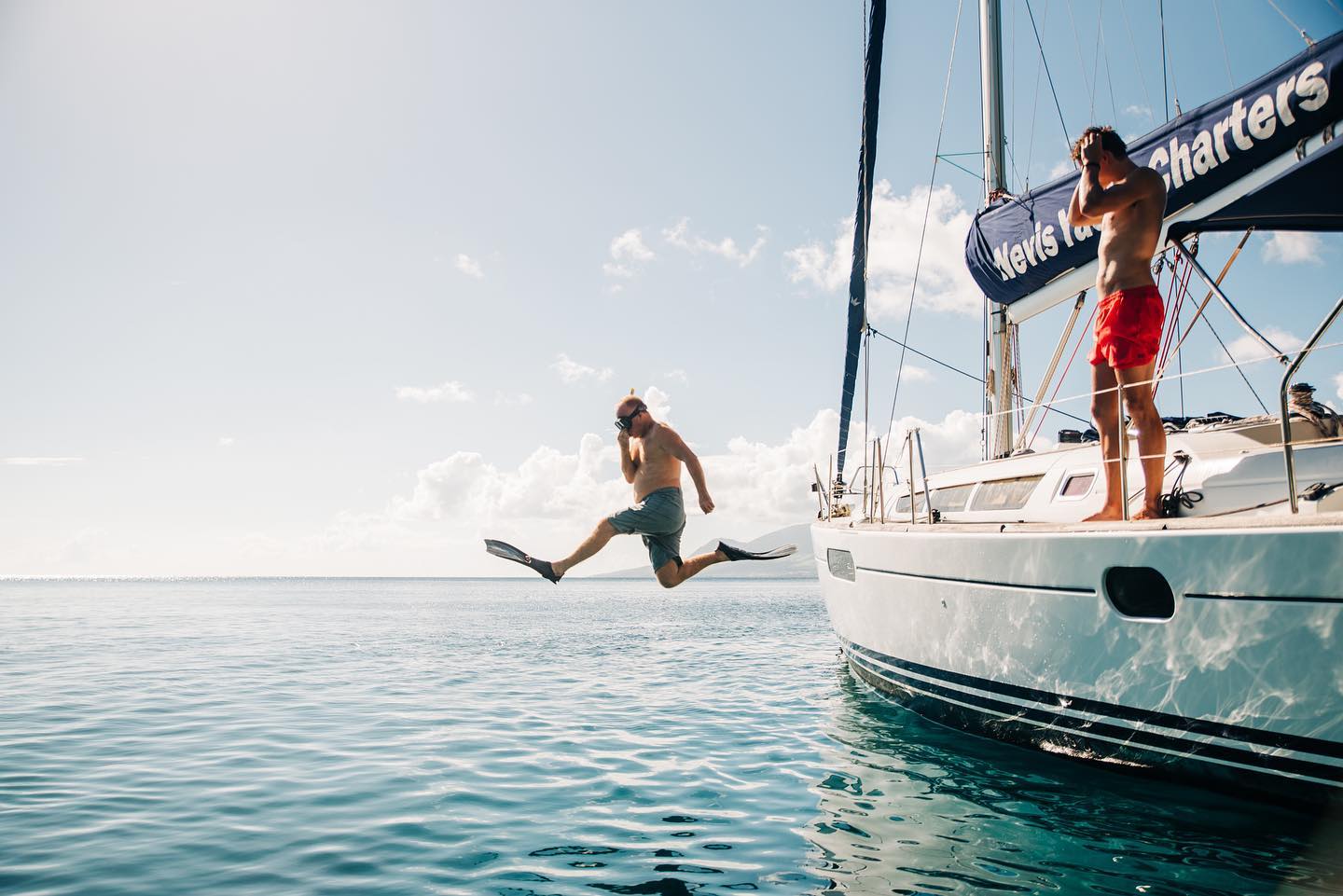 Person jumping off a boat into the ocean near Nevis with another person watching