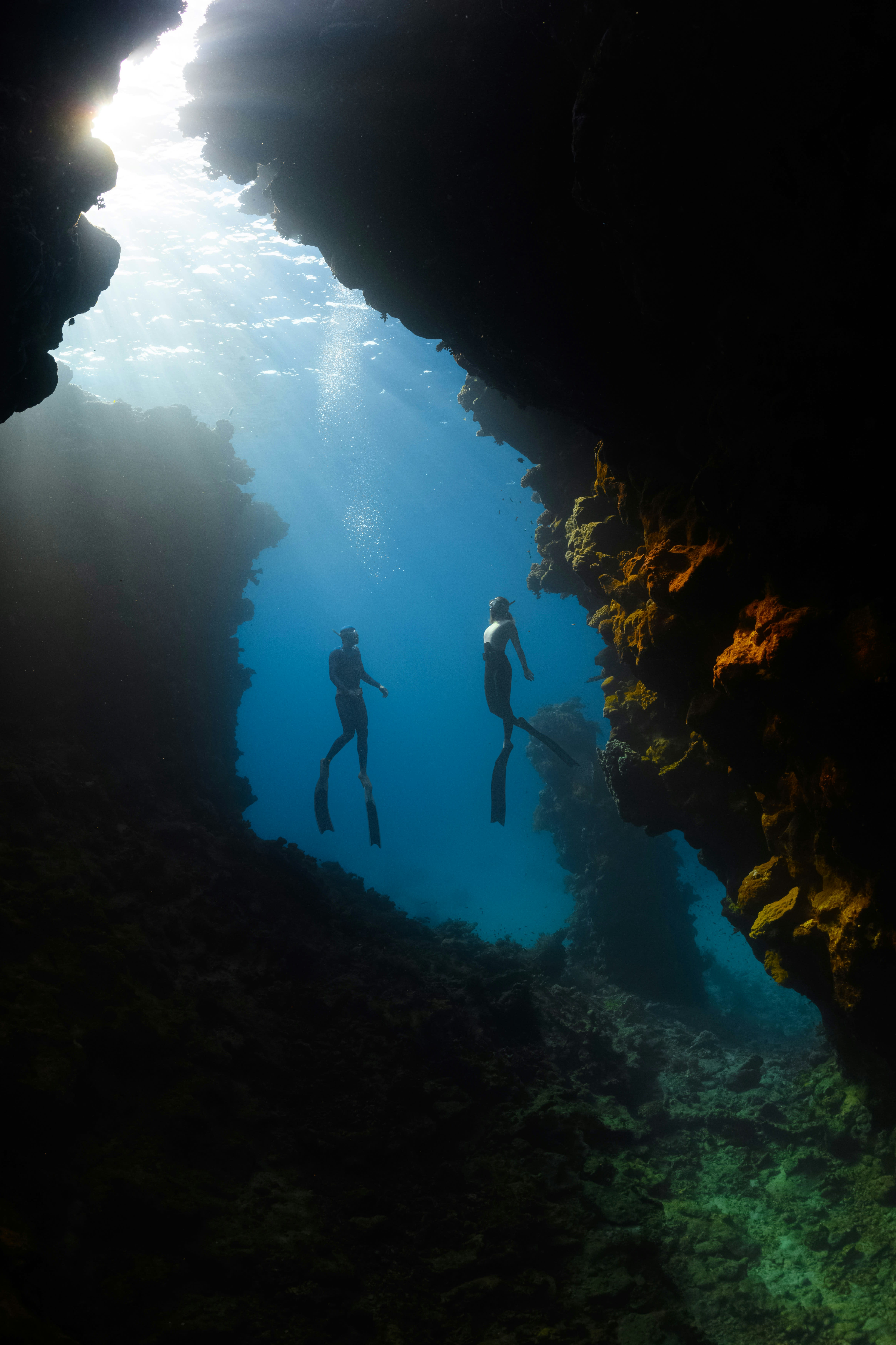 Two people snorkeling in an underwater cave near Nevis with sunlight streaming through the opening