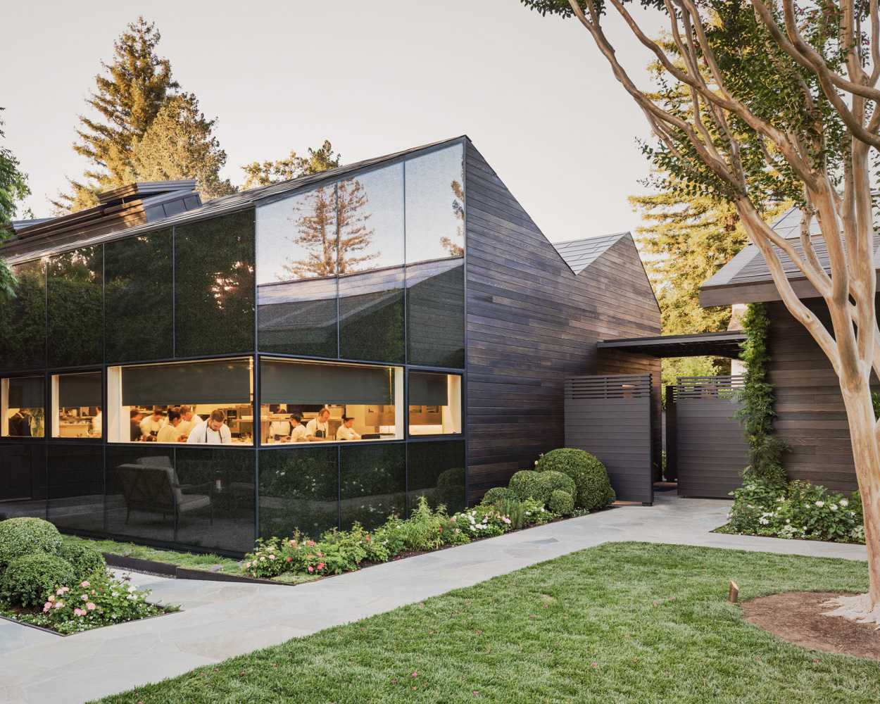 Exterior view of The French Laundry restaurant with chefs visible through large windows.