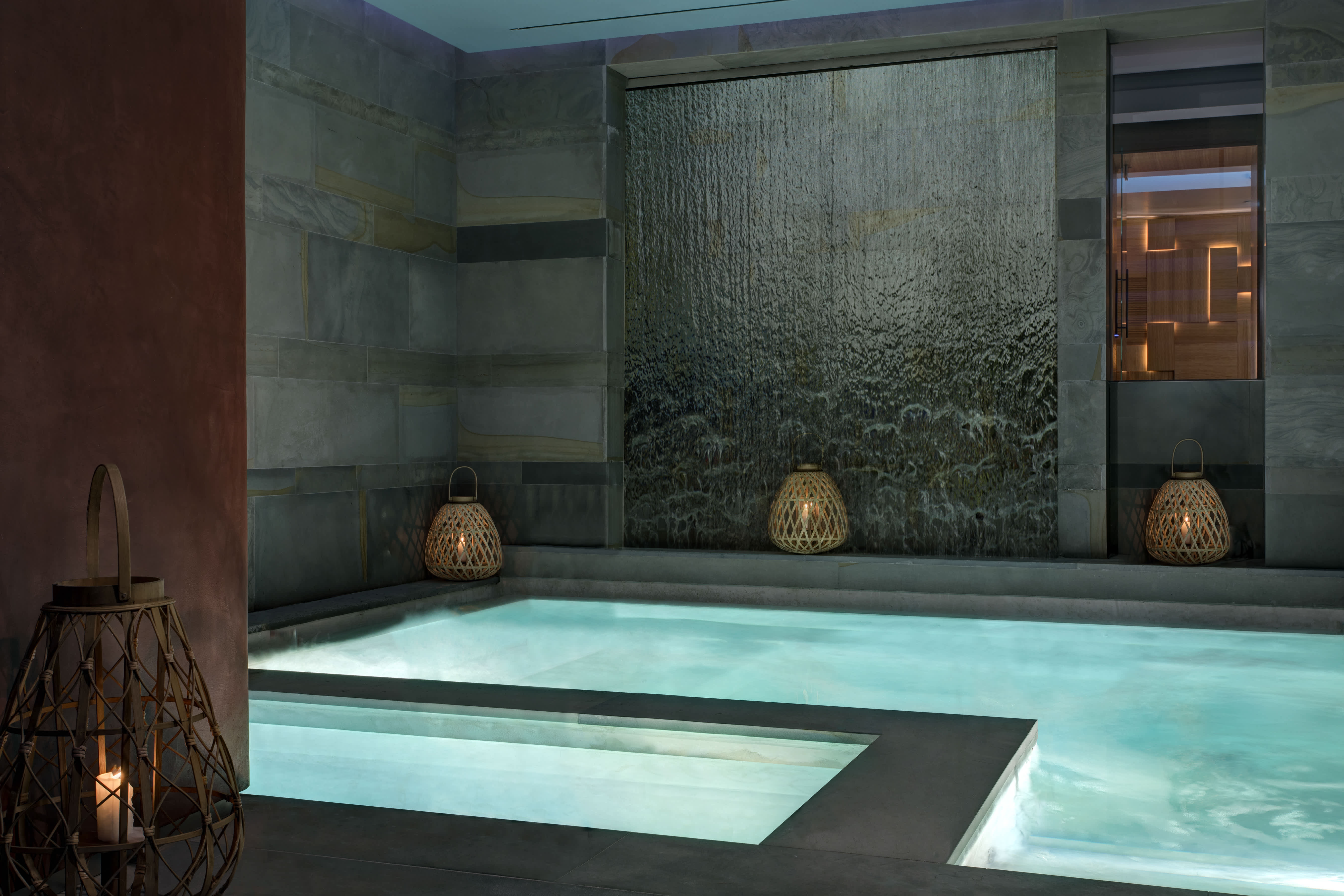 Indoor pool area with a cascading water feature and lanterns at Hotel de la Ville in Rome.