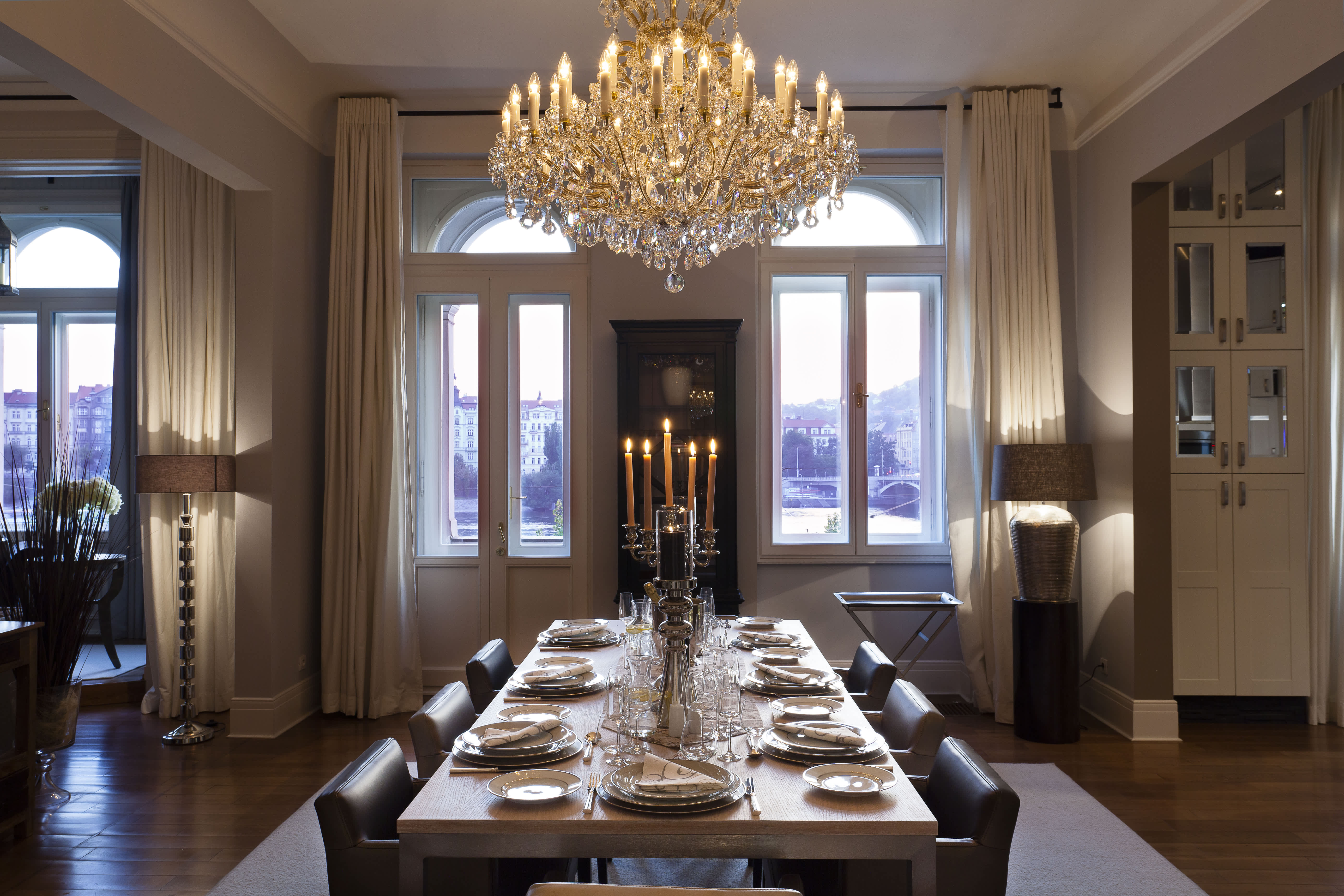Exclusive Resorts' private villa in Prague featuring an elegant dining room with a crystal chandelier, a beautifully set table, and large windows offering views of the city.