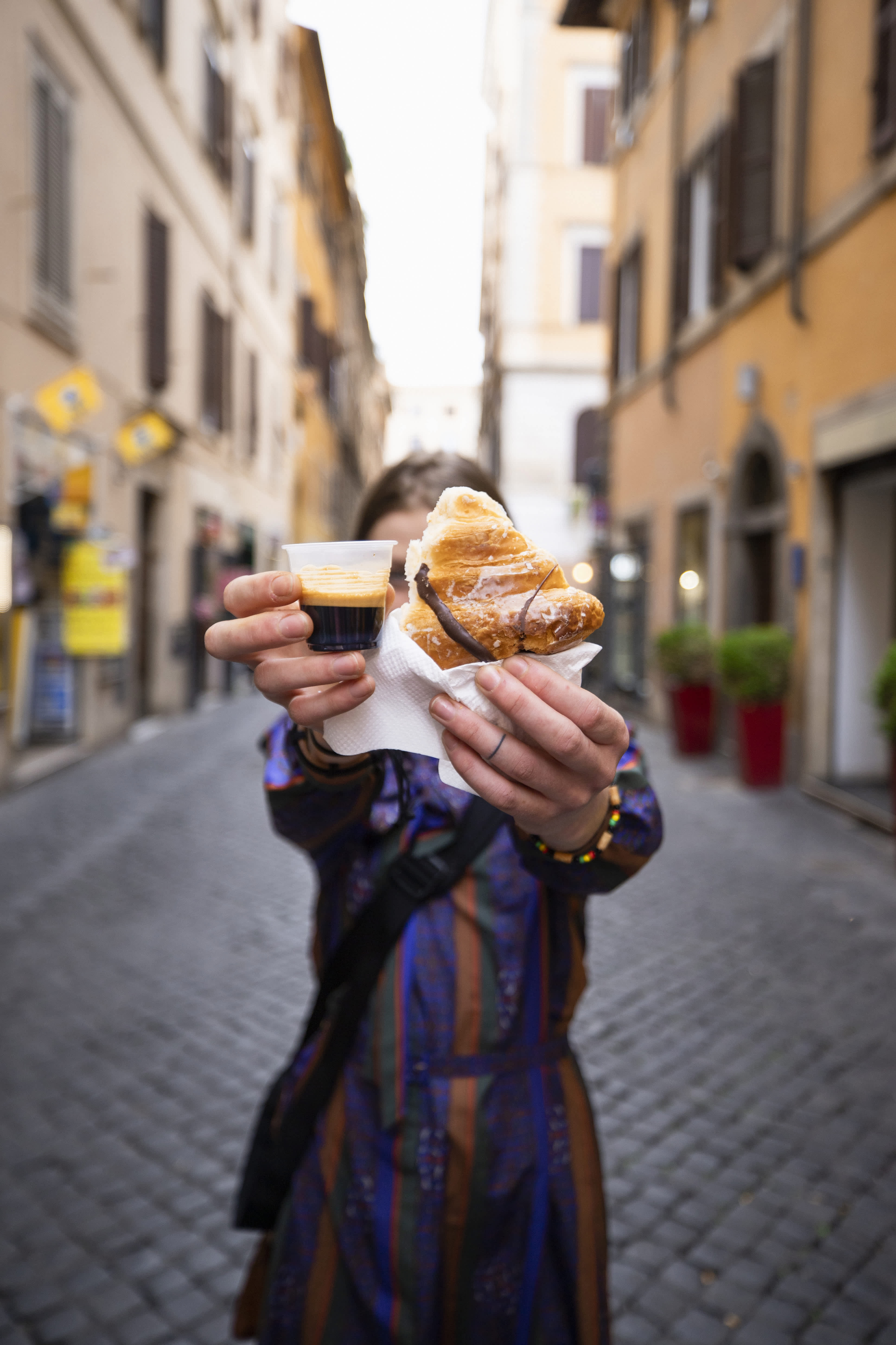 Person holding a croissant and espresso in a charming street in Rome