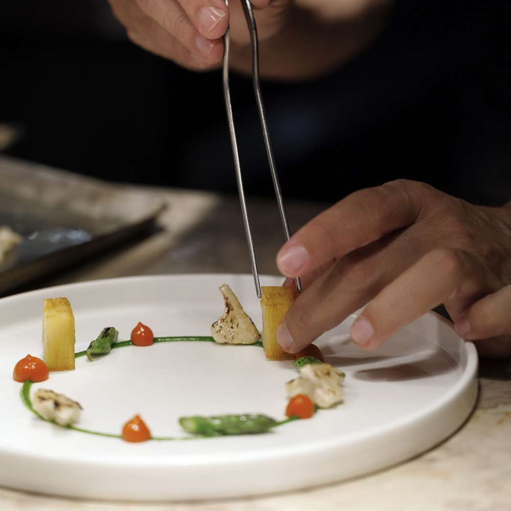 Chef plating a dish with vegetables and sauce dots on a white plate at Alma by Henrique Sá Pessoa in Lisbon, Portugal