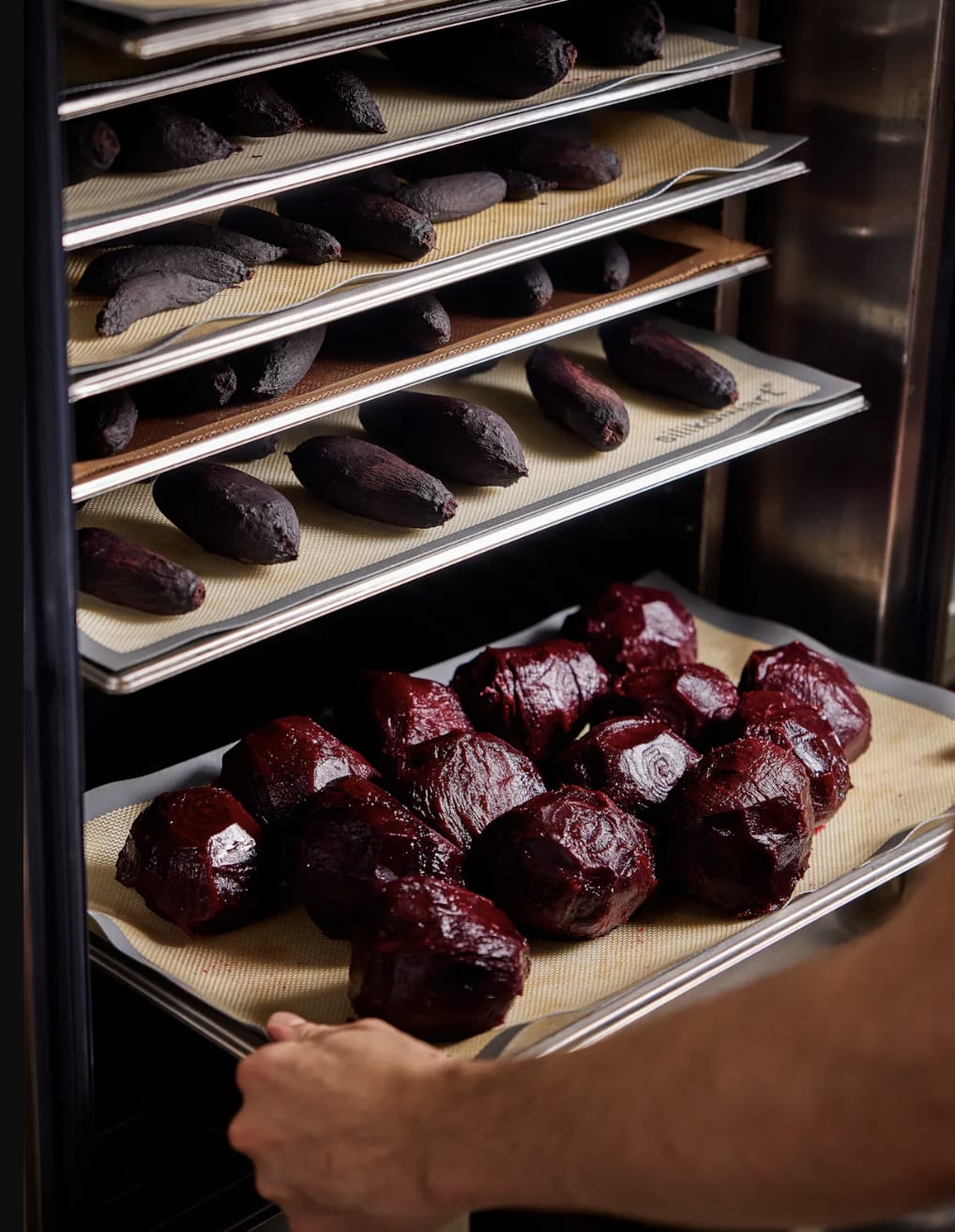 Person placing a tray of roasted vegetables into an oven at Degustation Restaurant in Prague