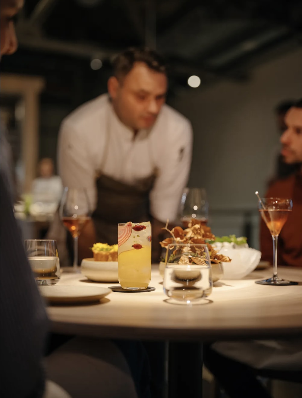 Table with drinks and dishes, with a chef talking to diners at Štangl Restaurant in Prague, Czech Republic.