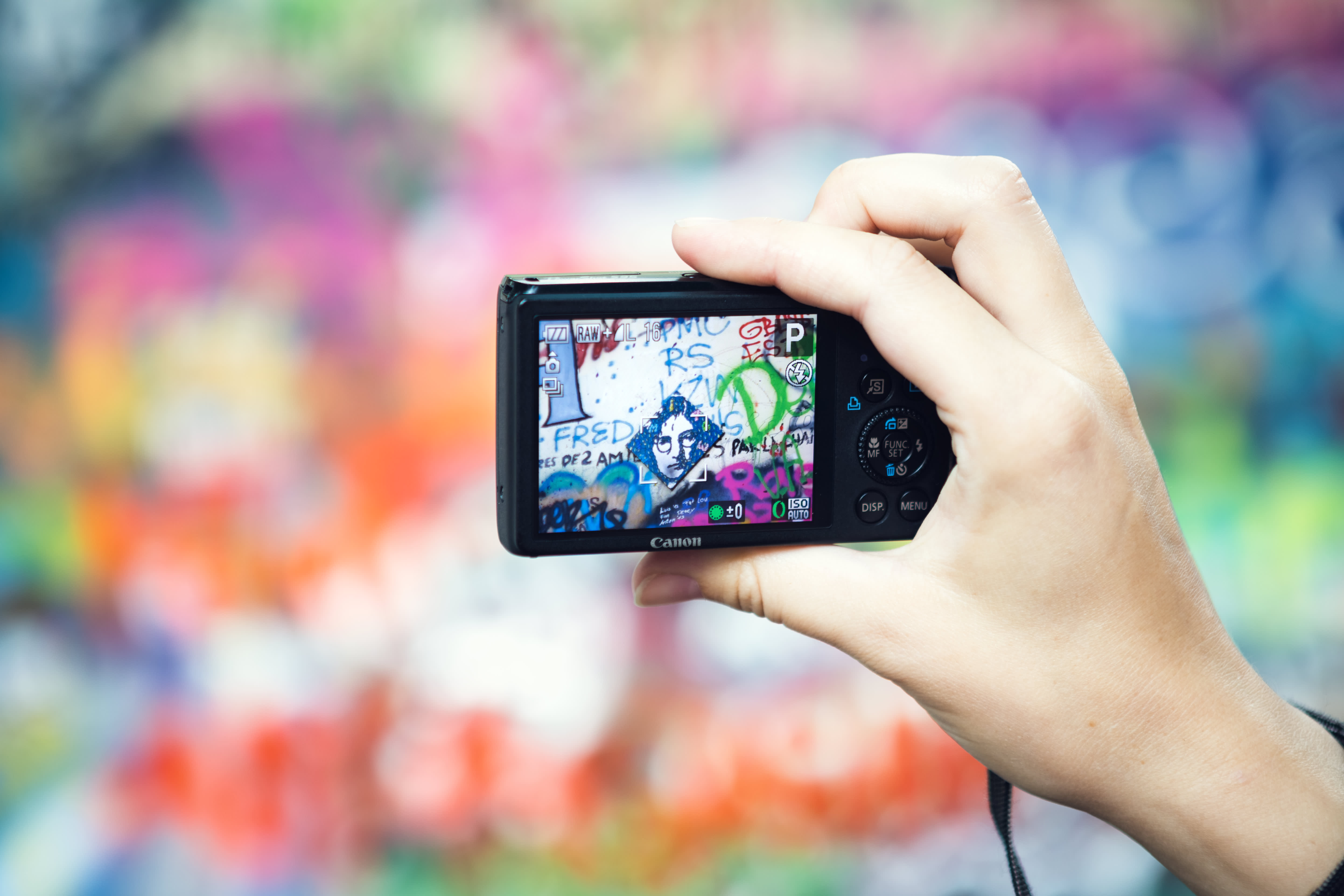 A person holding a camera capturing graffiti art on a colorful wall at the John Lennon Wall in Prague