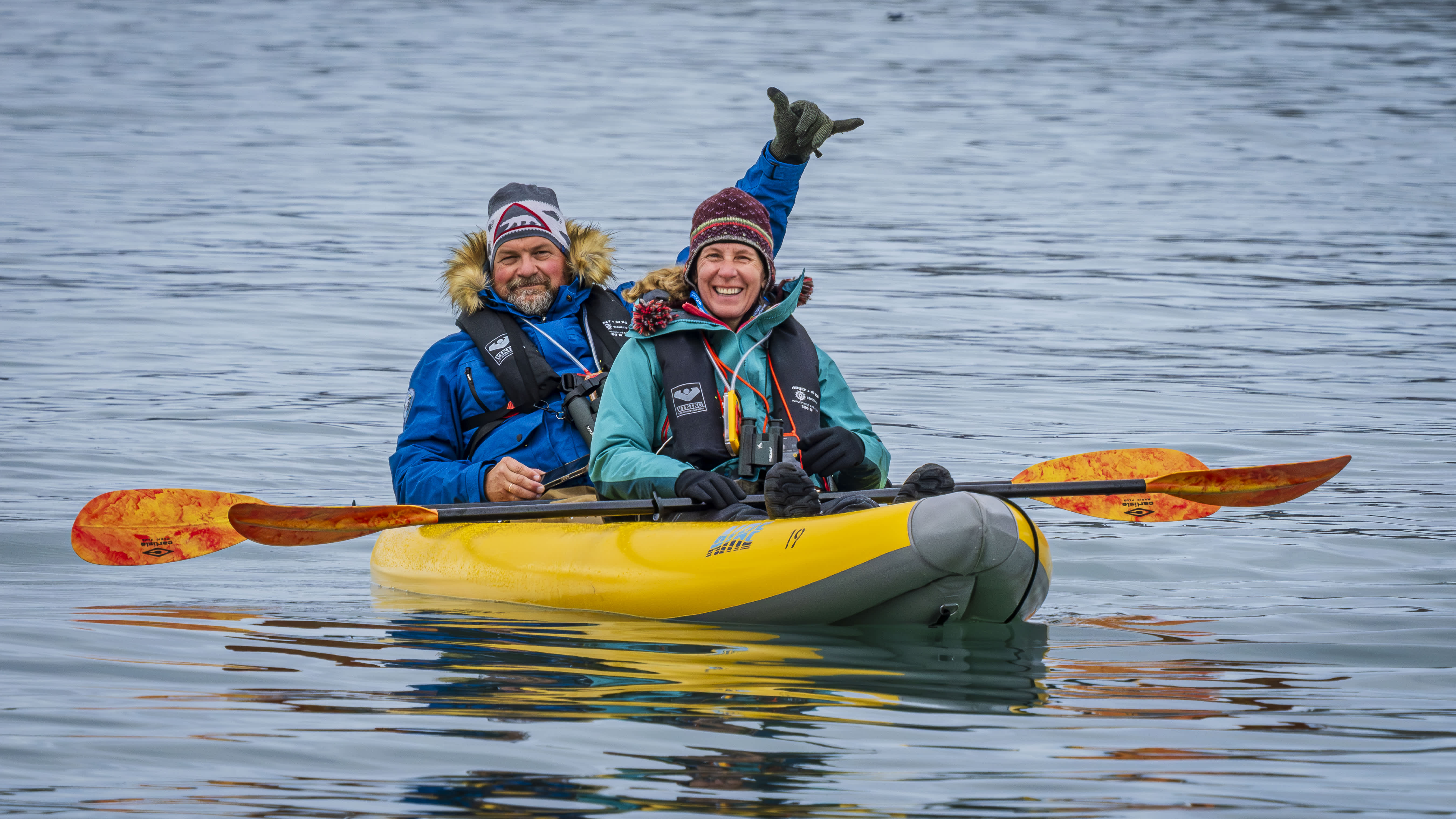 Exclusive Resorts' Members smiling and paddling in a yellow kayak on Arctic waters.