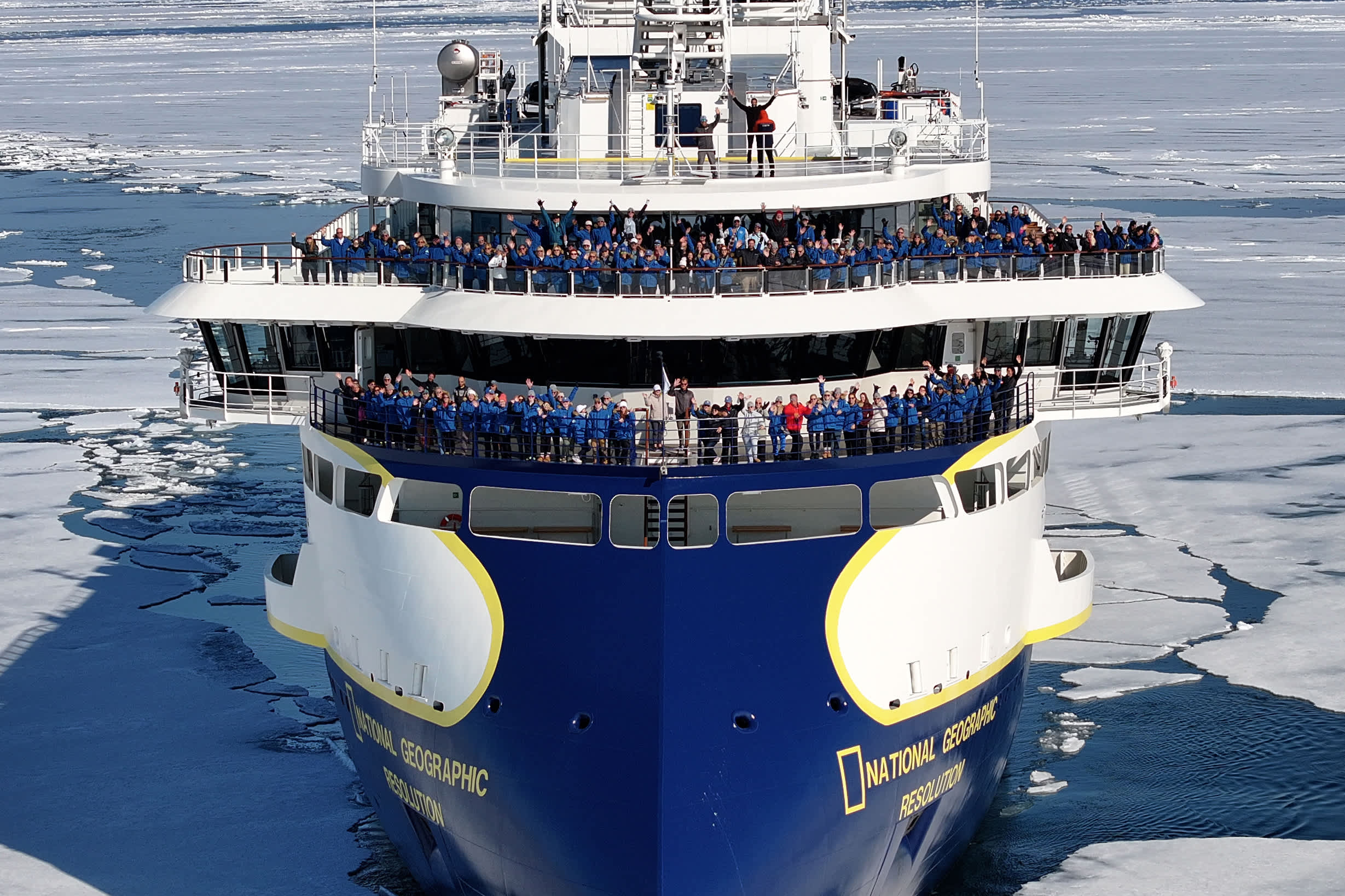 A large expedition ship, the National Geographic Resolution, filled with Exclusive Resorts' Members in blue jackets, navigating through the icy waters of the Arctic.