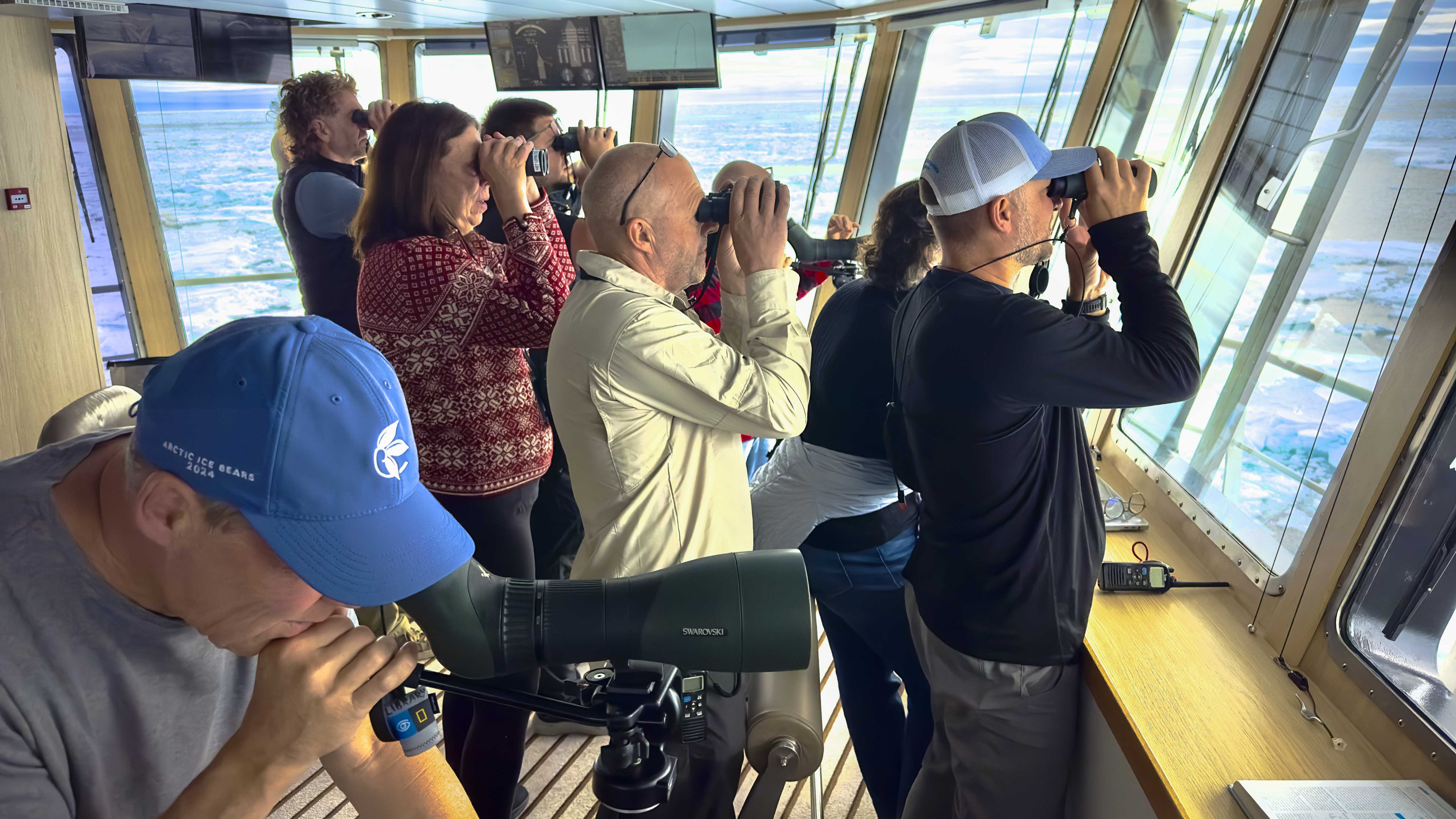 Exclusive Resorts' Members using binoculars to observe the Arctic landscape from inside a ship's observation deck.