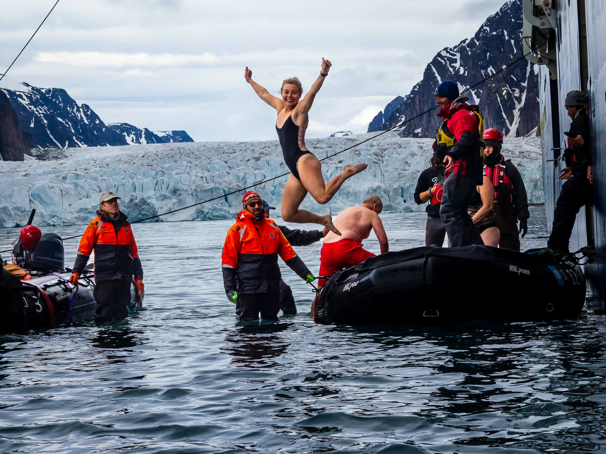 An Exclusive Resorts Member jumping off a boat into icy waters with snowy mountains in the background in Antarctica.
