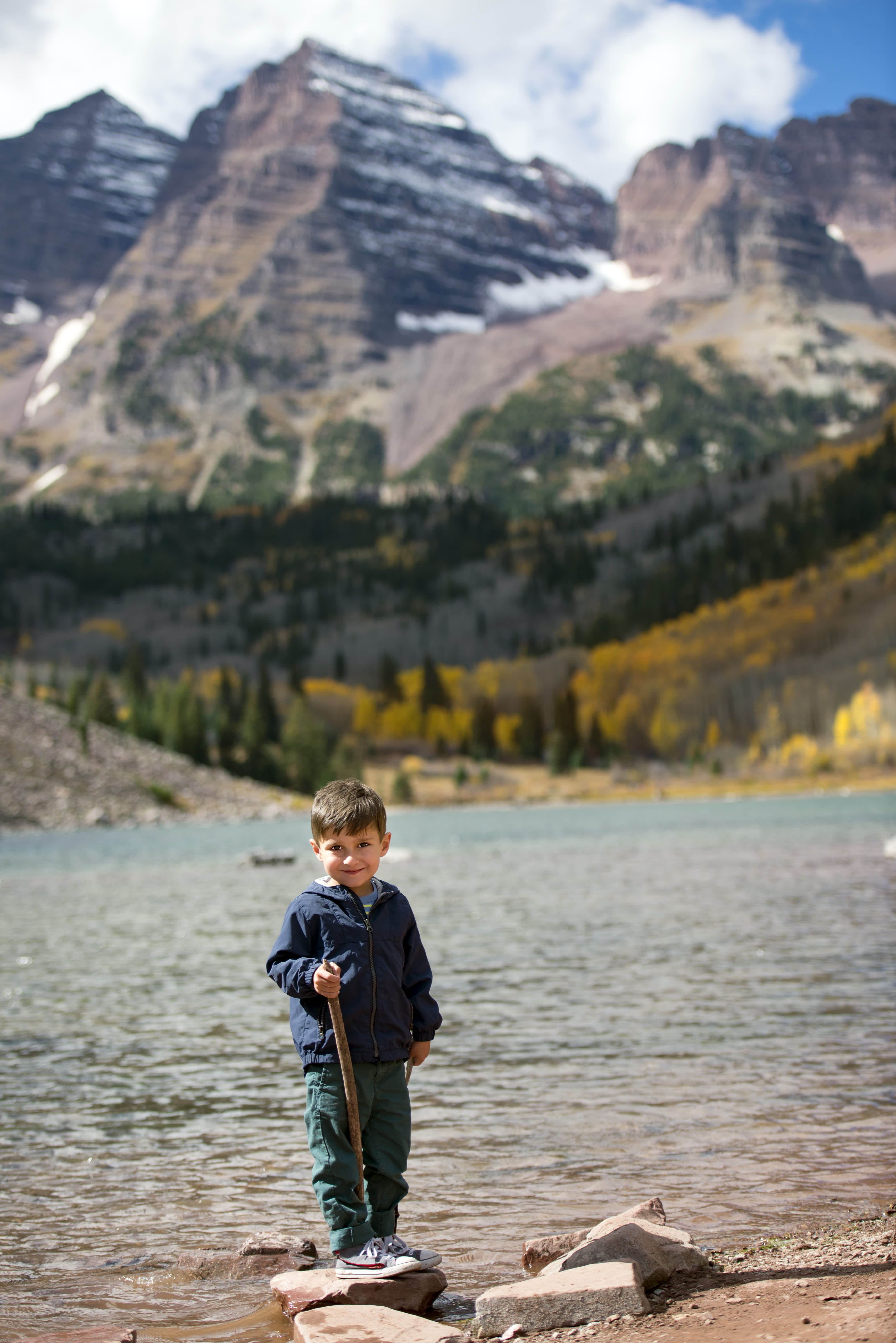 A young boy smiling with the Maroon Bells mountain range in the background during autumn.