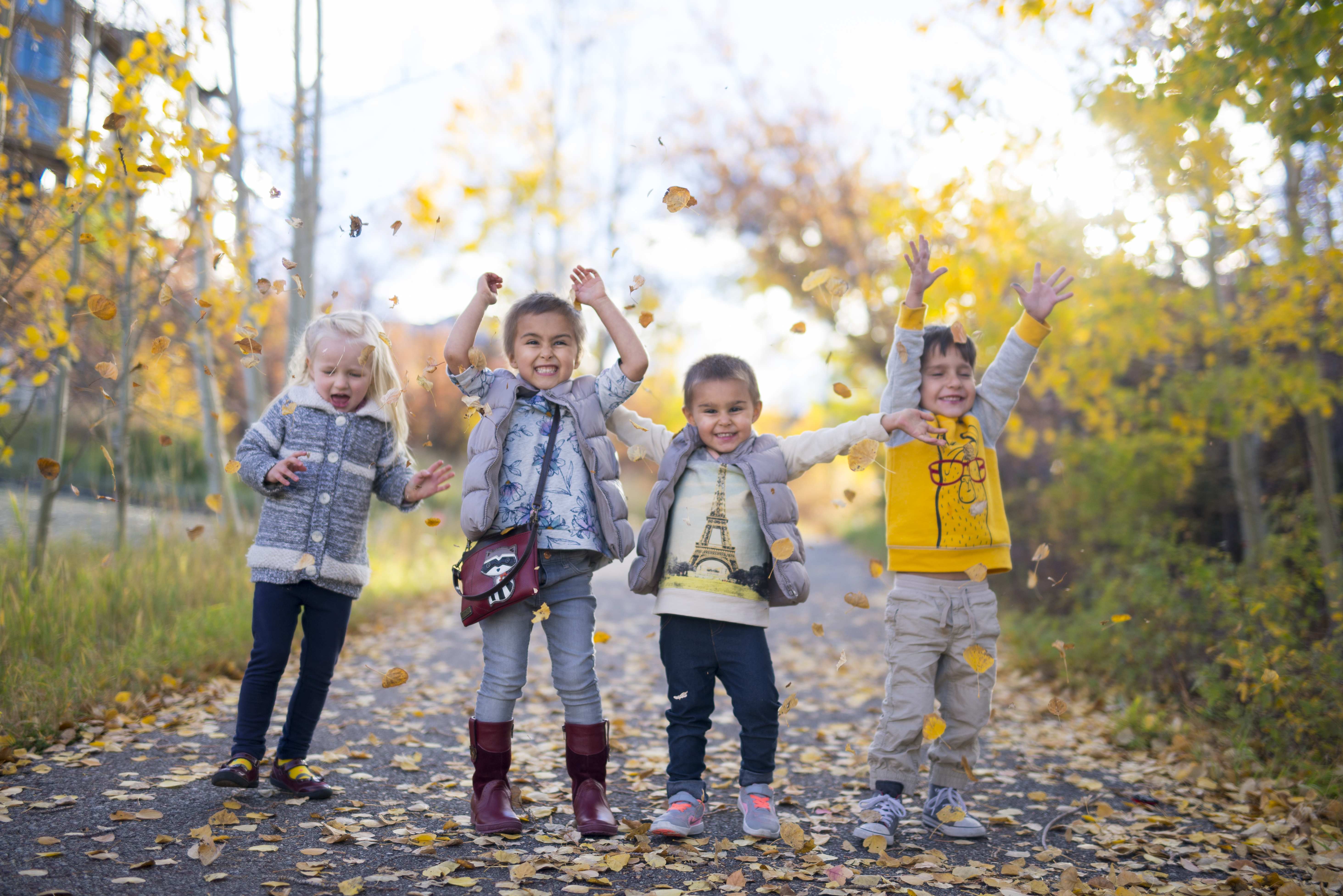 Children playing with falling leaves on a sunny walking trail in Colorado during autumn.