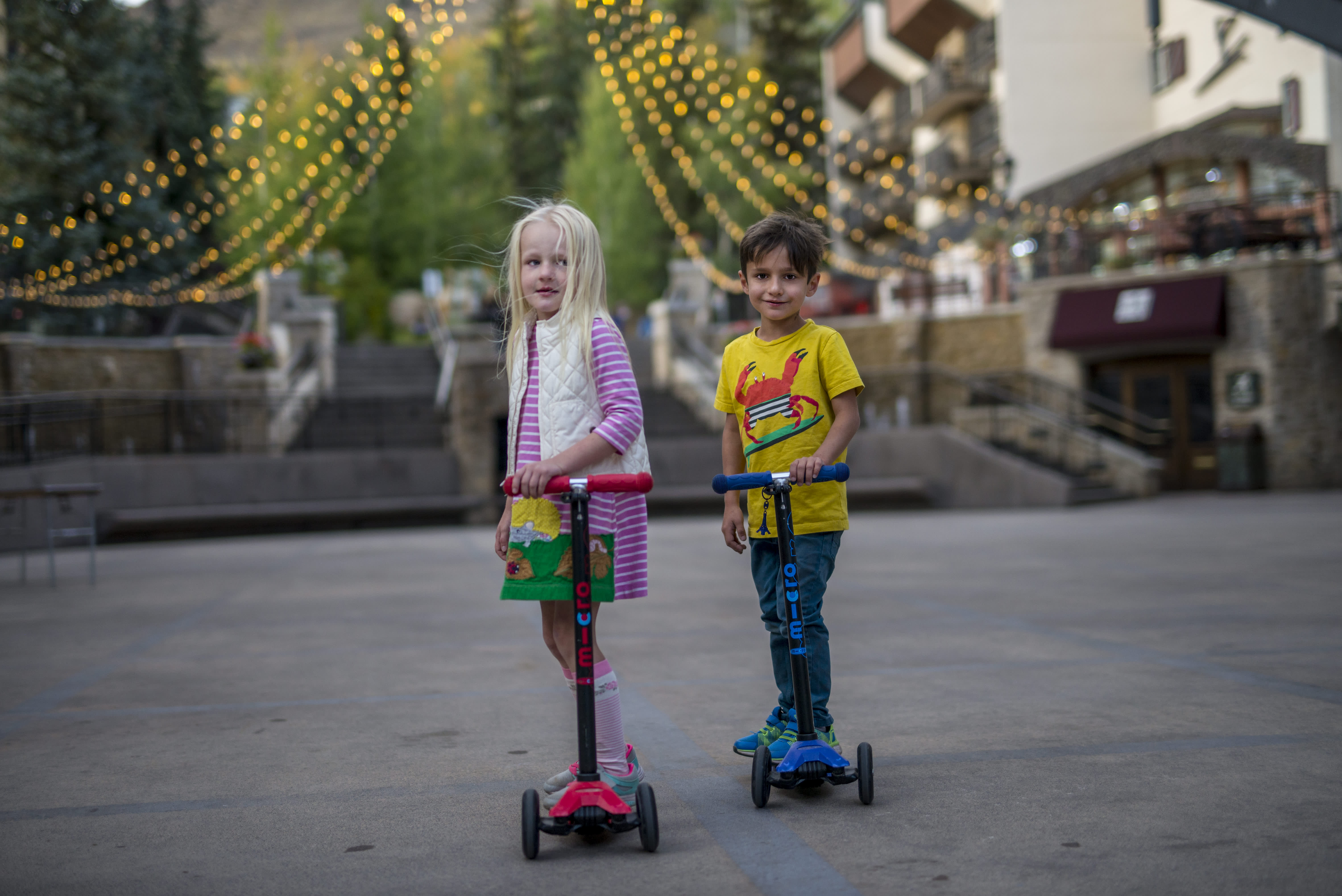 Two children on scooters in the center of The Arrabelle at Vail Square.