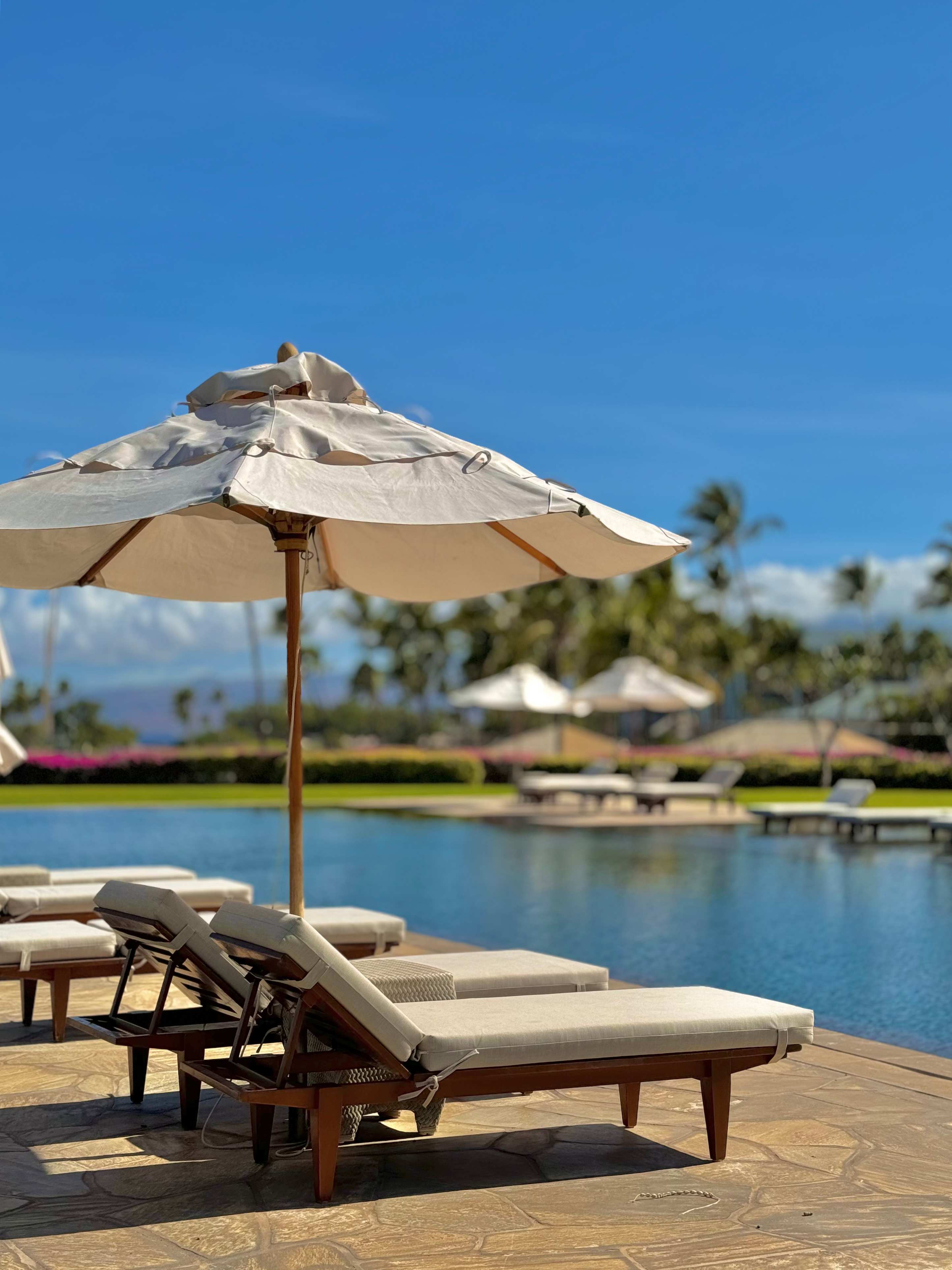 Poolside lounge chairs and umbrellas at Pauoa Beach Club on the Kohala Coast.