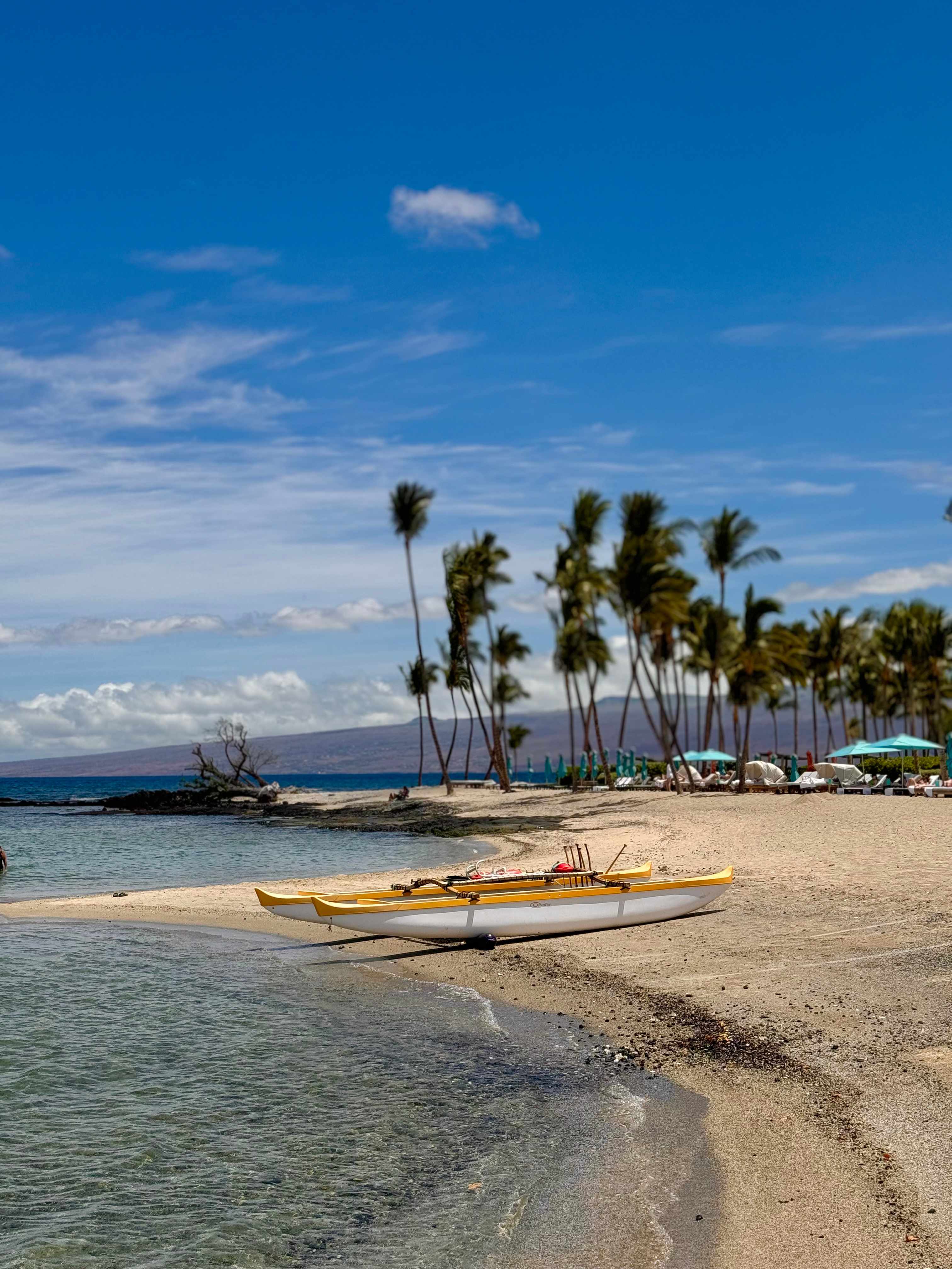 An outrigger canoe resting on the sandy shore of the Kohala Coast.