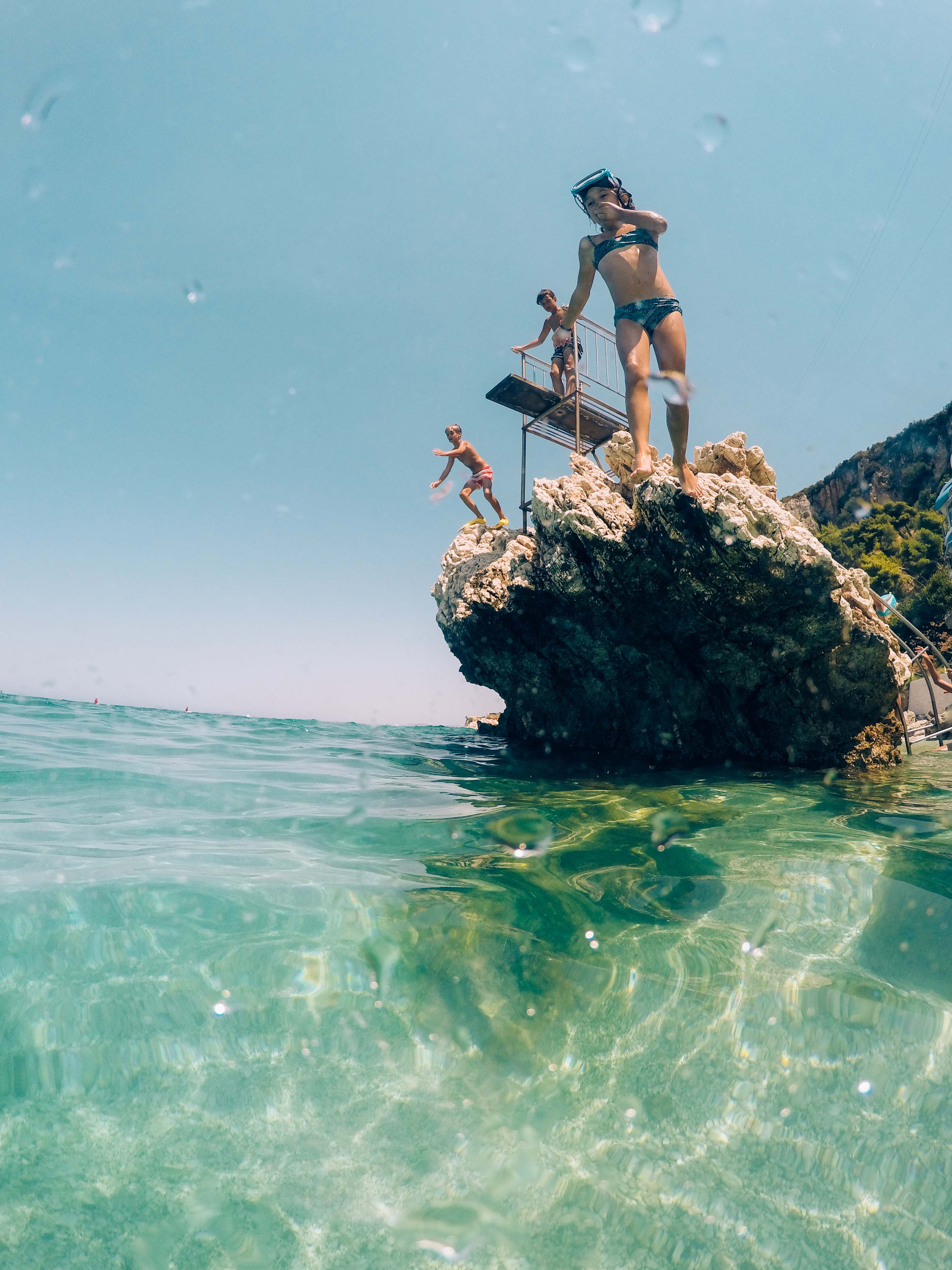 People cliff diving into the clear blue waters of Corfu on a sunny day