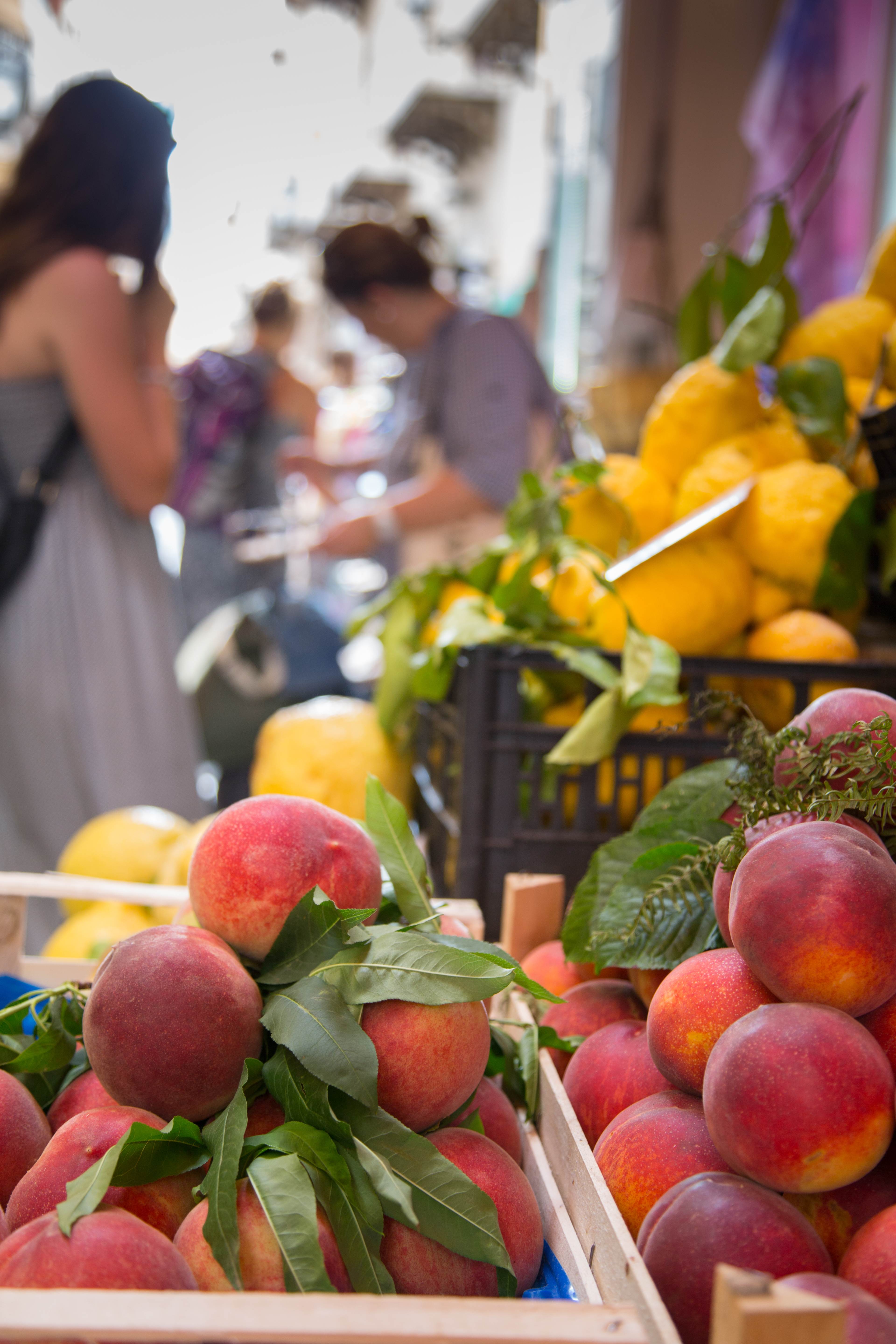 Fresh peaches and lemons displayed at a market with people shopping in the background.