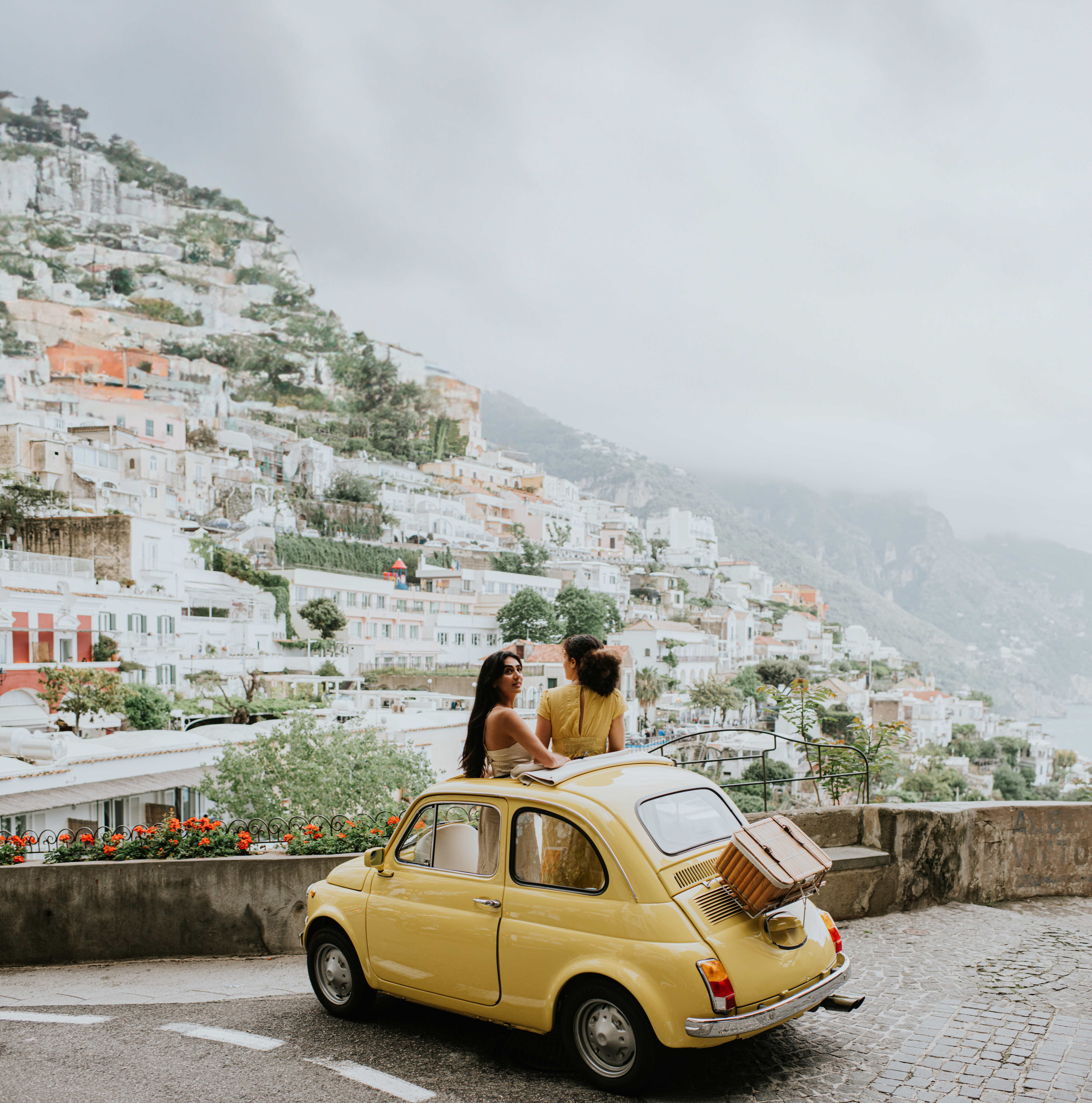 Couple enjoying scenic view of Positano from a yellow car on the Amalfi Coast.