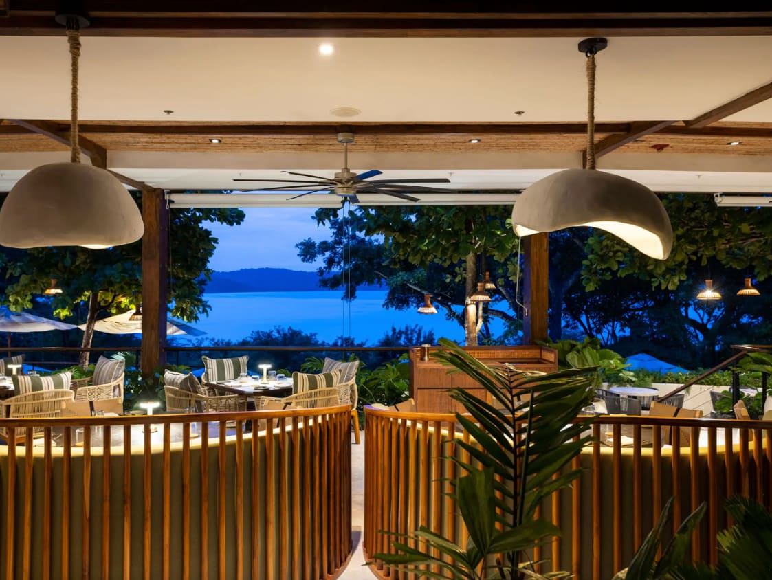 Dining area at Ostra restaurant in Costa Rica with a view of the ocean at dusk, featuring elegant decor and warm lighting.