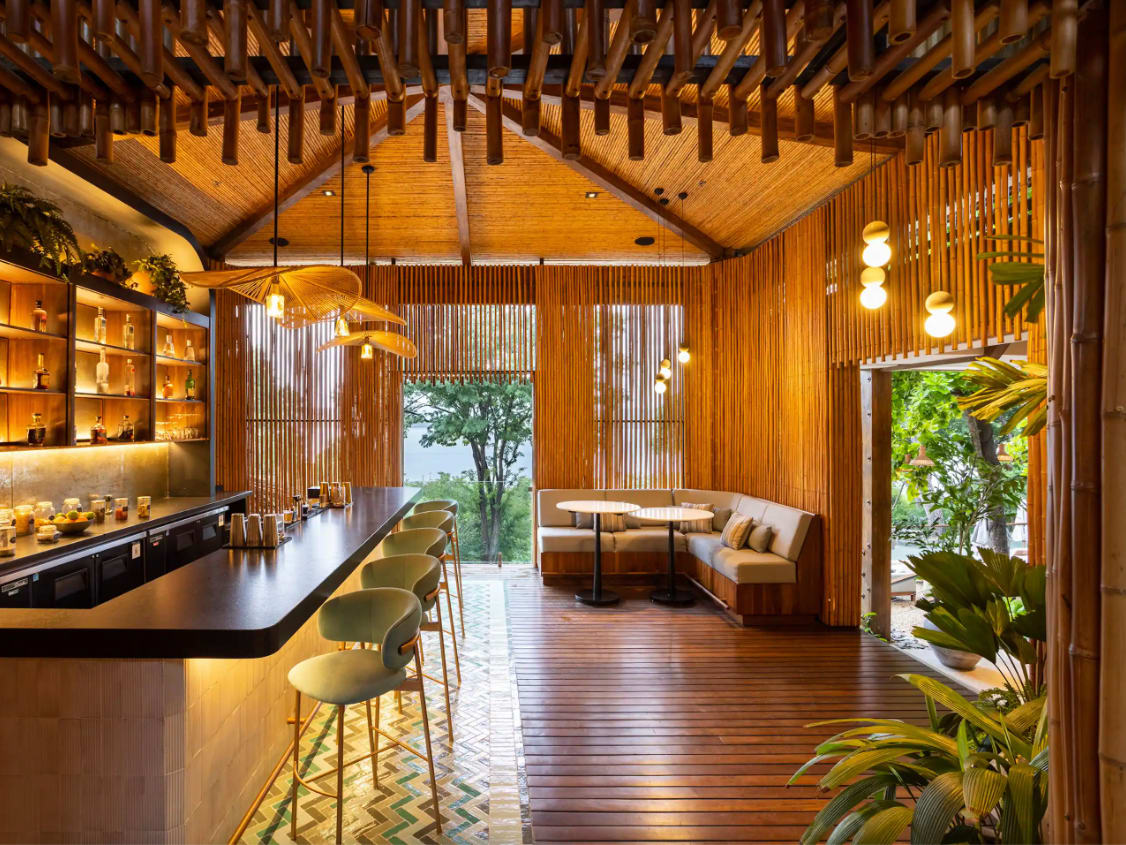 Ostra Bar in Costa Rica with warm wooden interiors, a stylish bar, and seating area overlooking lush greenery.