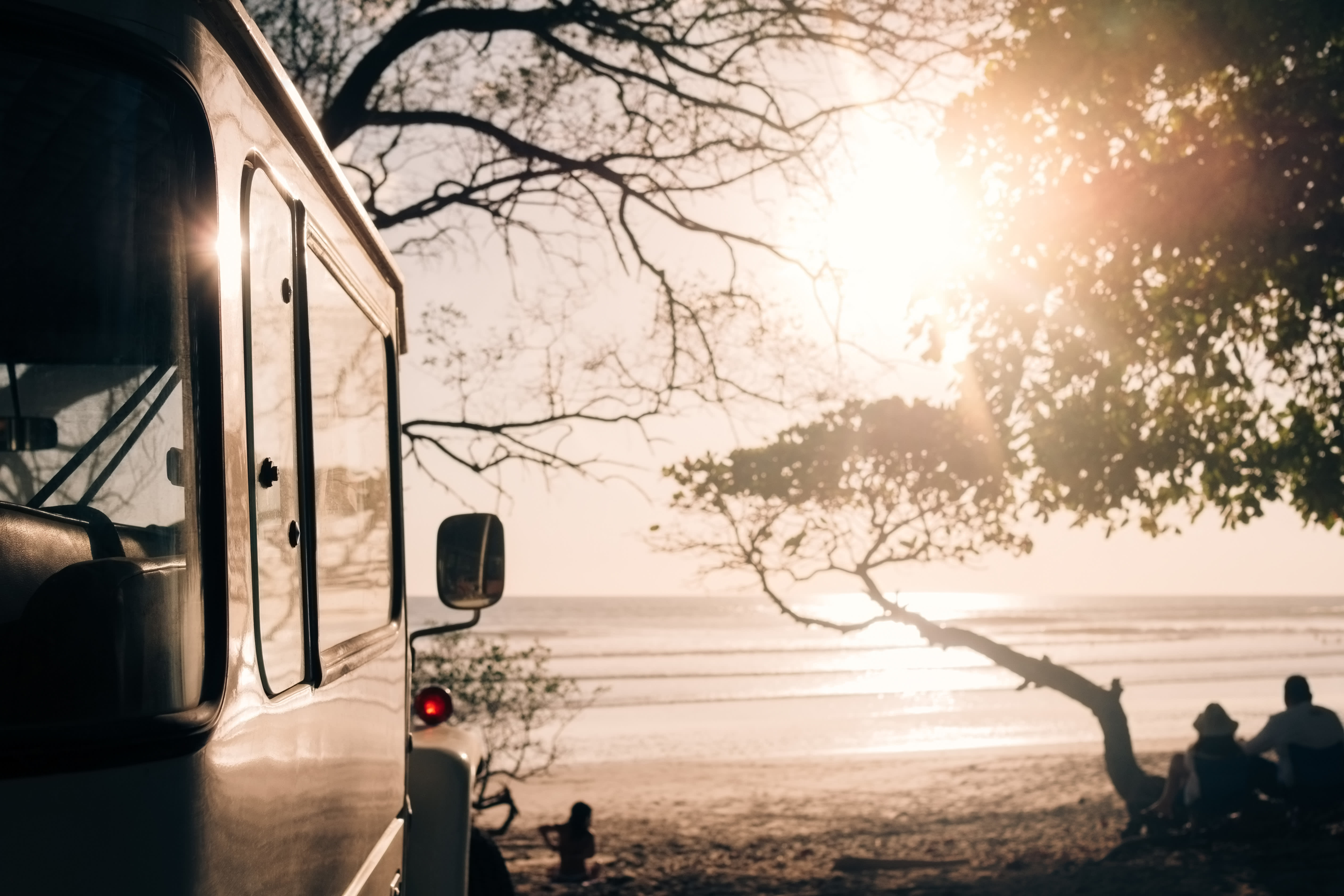 4x4 vehicle parked on a beach at sunset in Costa Rica with people relaxing under a tree, capturing the essence of an adventurous tour.
